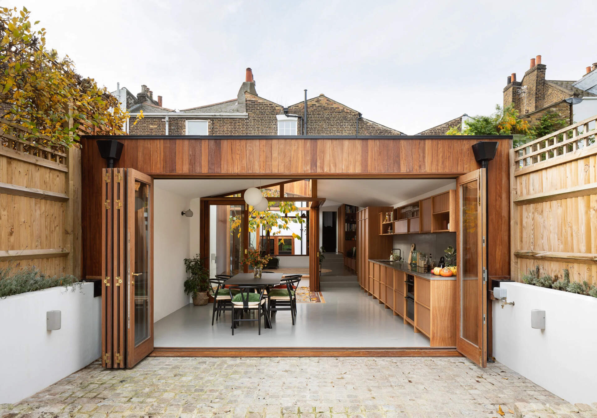 A modern wood extension with a green roof opens a Georgian home to the backyard with large folding glass doors.