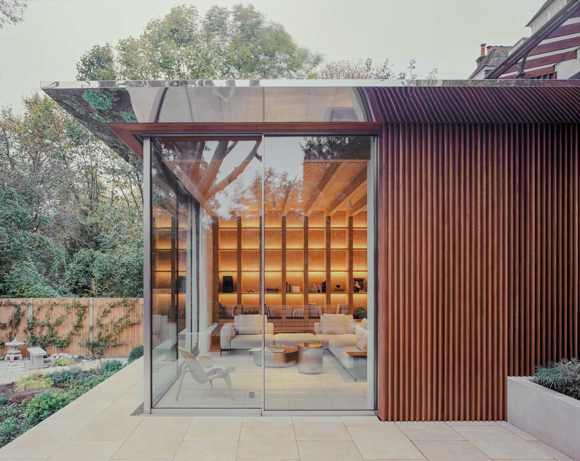 A seamless glass corner opens fully to the garden, creating uninterrupted views and a strong indoor-outdoor connection.