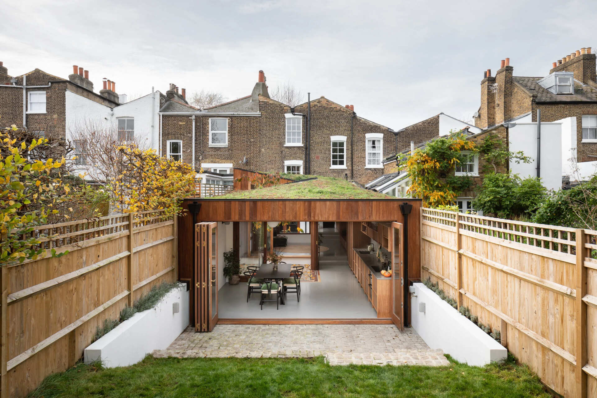 A modern wood extension with a green roof opens a Georgian home to the backyard with large folding glass doors.