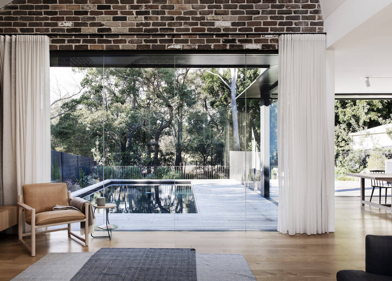 An open-plan living space combines a brick fireplace, custom wood cabinetry, and clean lines for a warm modern interior.