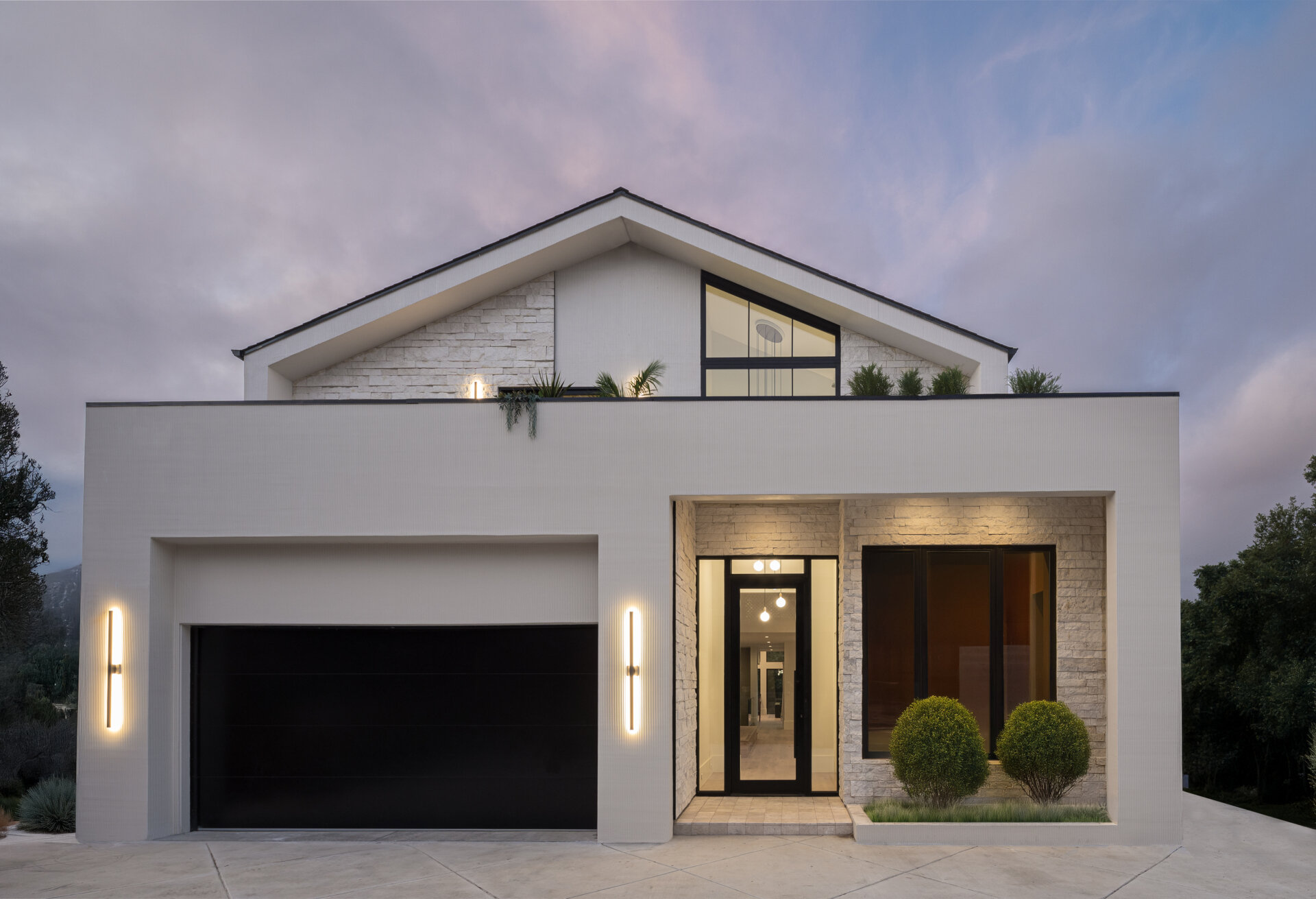 A modern home exterior in stucco and limestone uses texture and light to create depth on a narrow sloped lot.