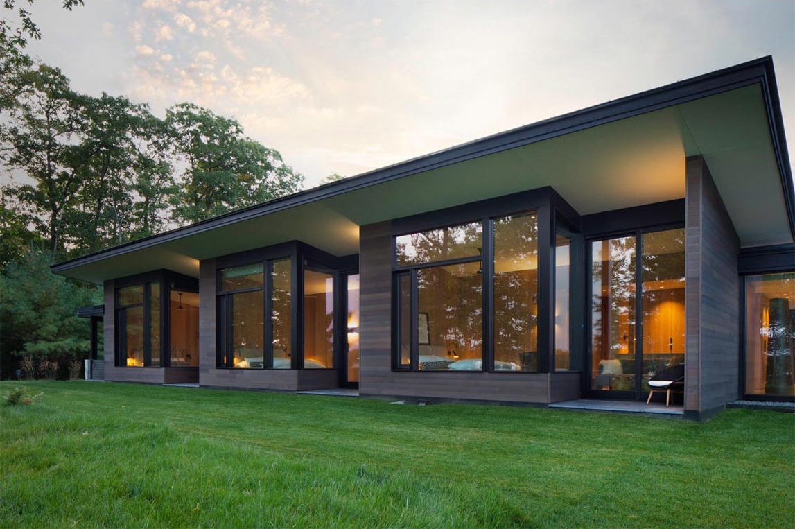 Es una casa de huéspedes moderna de Wisconsin con piedra tosca, amplias paredes de vidrio y vistas panorámicas del lago rodeado por el bosque circundante.