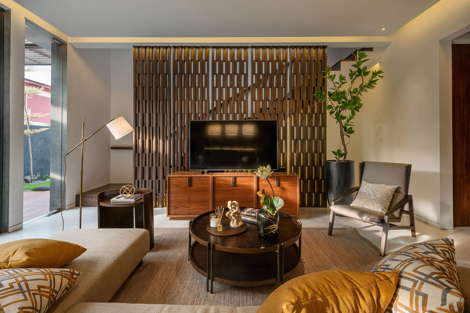 The living room is anchored by artistic panels that partially conceal the staircase behind them. These panels double as a backdrop for the television, turning a functional feature into a design focal point.