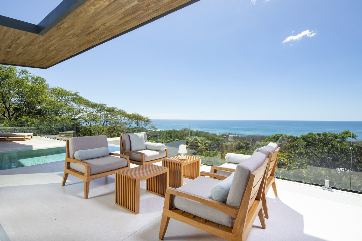 An open plan living space with a floating wood ceiling and sliding glass walls that open fully to a shaded balcony.