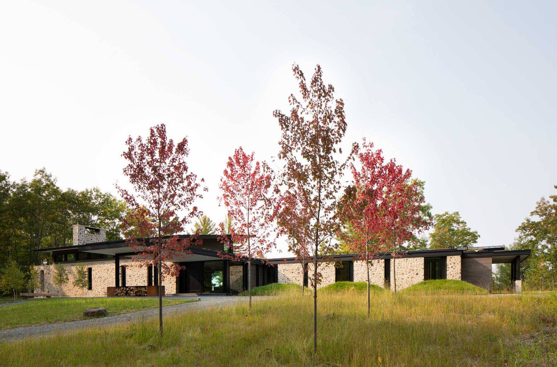 Es una casa de huéspedes moderna de Wisconsin con piedra tosca, amplias paredes de vidrio y vistas panorámicas del lago rodeado por el bosque circundante.