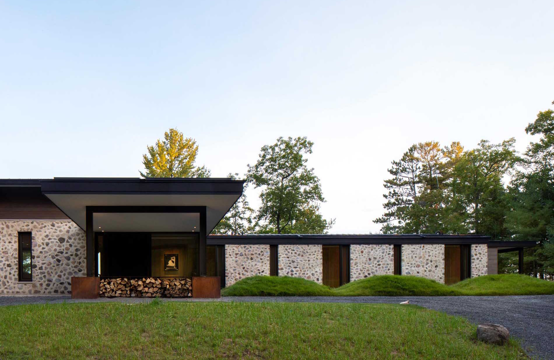 Es una casa de huéspedes moderna de Wisconsin con piedra tosca, amplias paredes de vidrio y vistas panorámicas del lago rodeado por el bosque circundante.