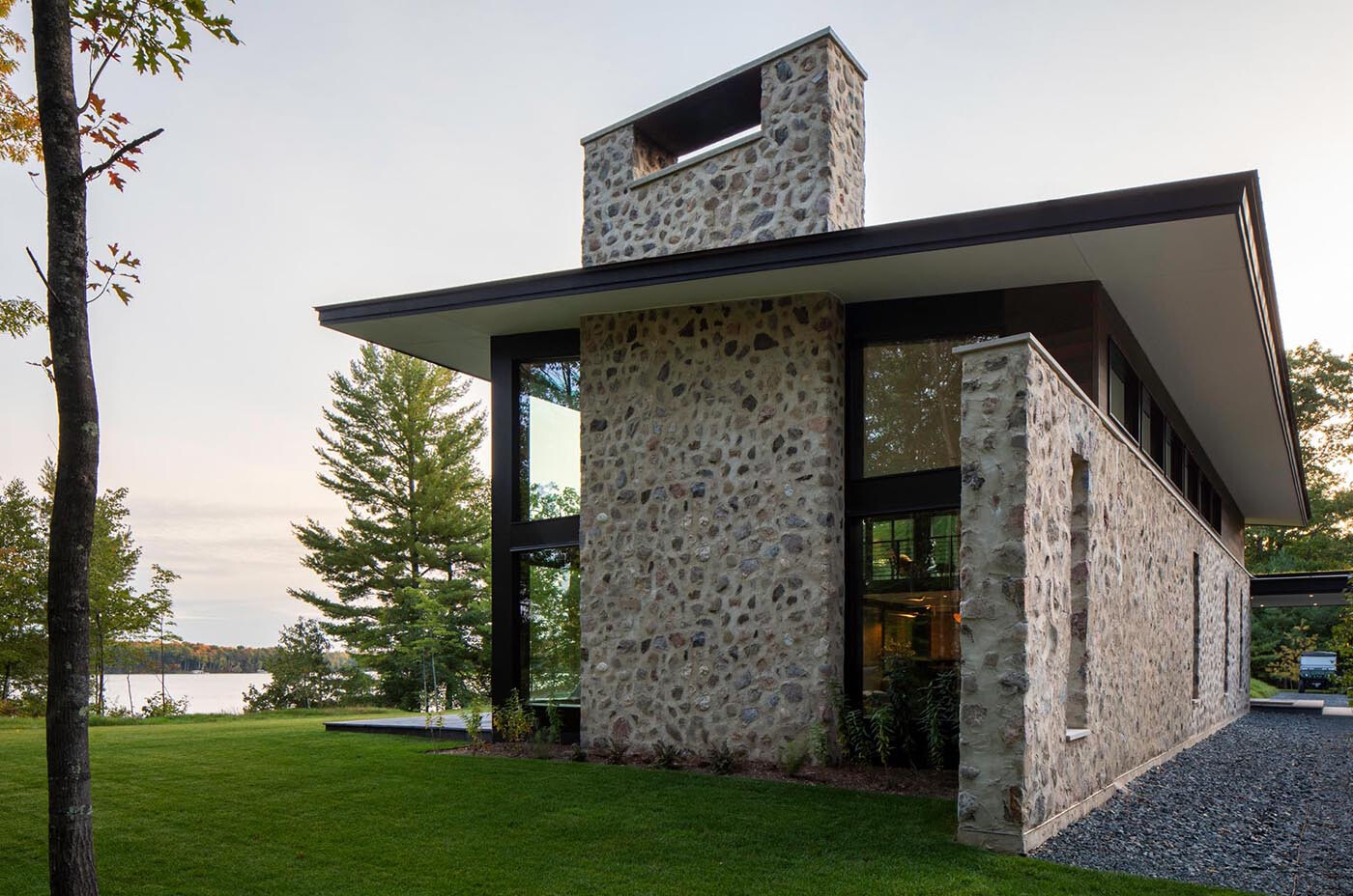Es una casa de huéspedes moderna de Wisconsin con piedra tosca, amplias paredes de vidrio y vistas panorámicas del lago rodeado por el bosque circundante.