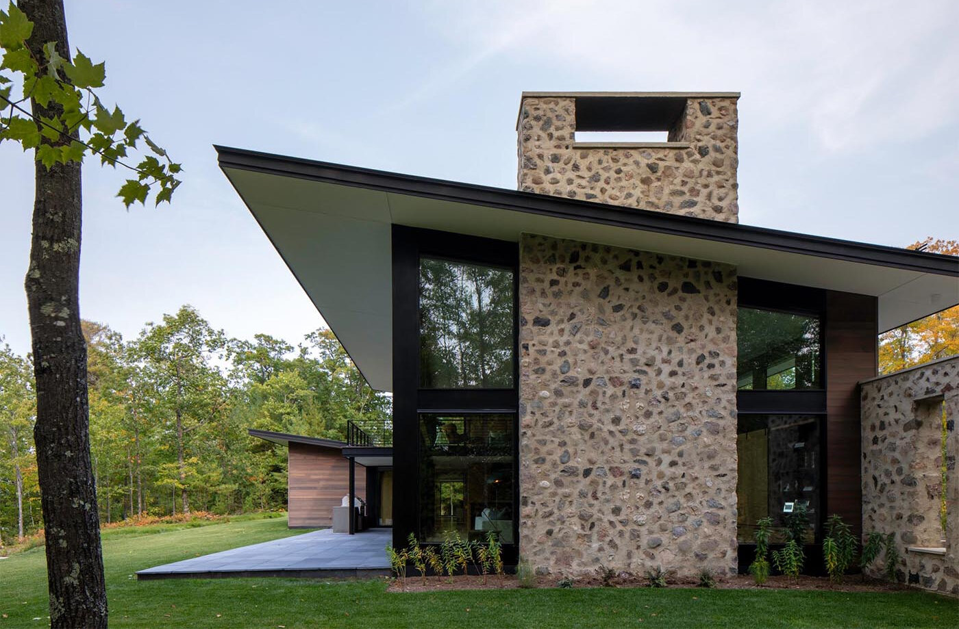 Es una casa de huéspedes moderna de Wisconsin con piedra tosca, amplias paredes de vidrio y vistas panorámicas del lago rodeado por el bosque circundante.