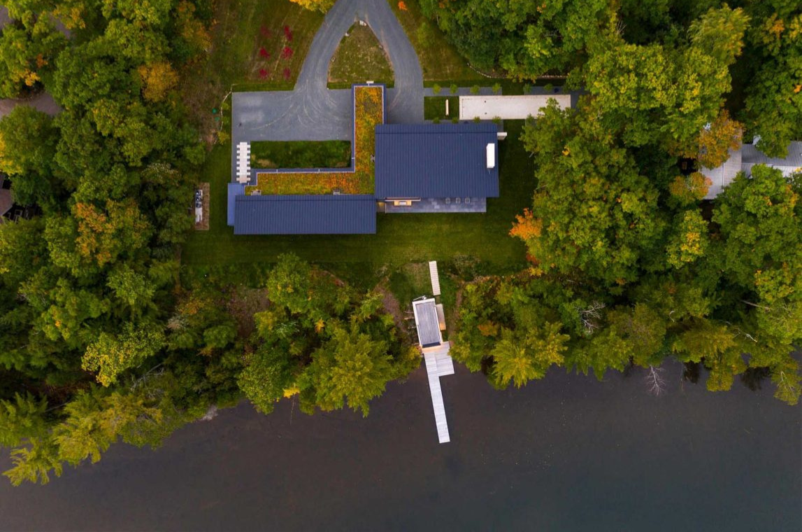 Es una casa de huéspedes moderna de Wisconsin con piedra tosca, amplias paredes de vidrio y vistas panorámicas del lago rodeado por el bosque circundante.