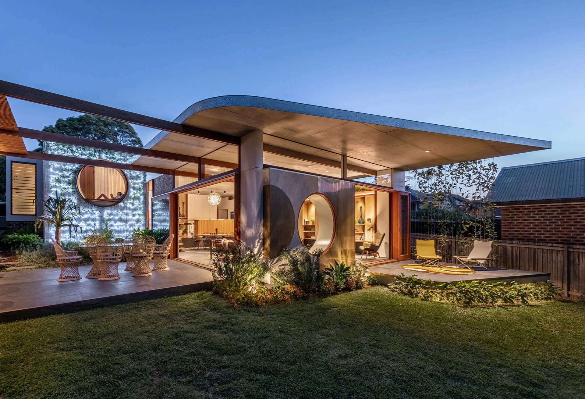 Esta moderna casa de Sydney presenta una línea de techo curva que brilla por la noche, reflejando la luz en el interior y creando una característica arquitectónica cálida.