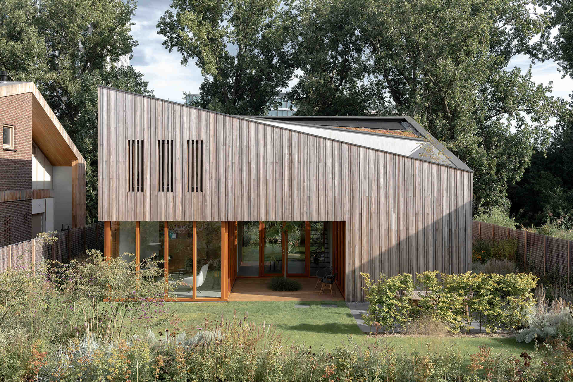 This Rotterdam home features a sculptural shape with wood siding, softened by surrounding gardens and selective openings.