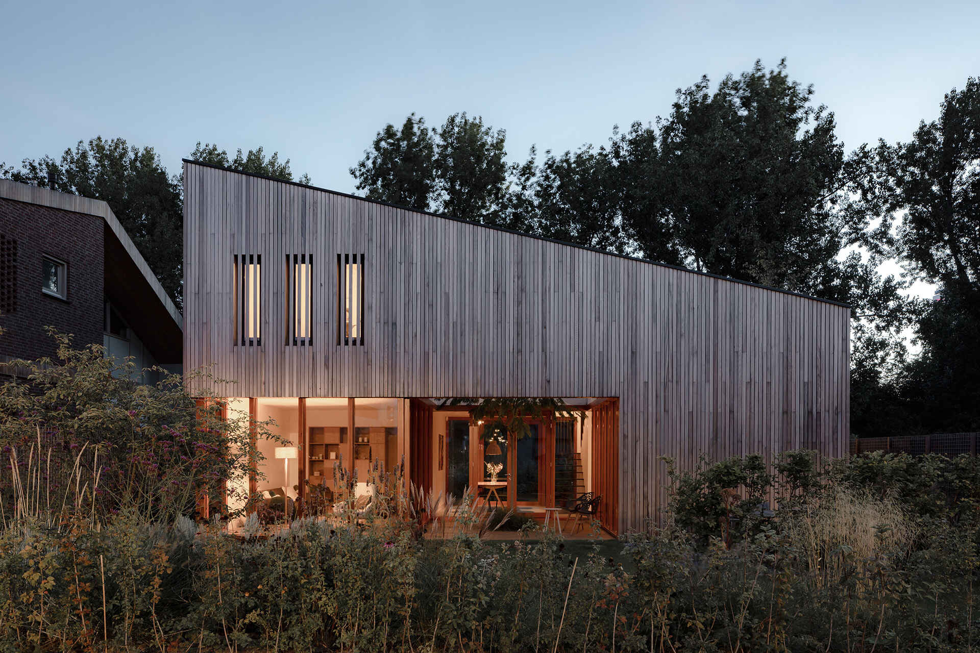 This Rotterdam home features a sculptural shape with wood siding, softened by surrounding gardens and selective openings.