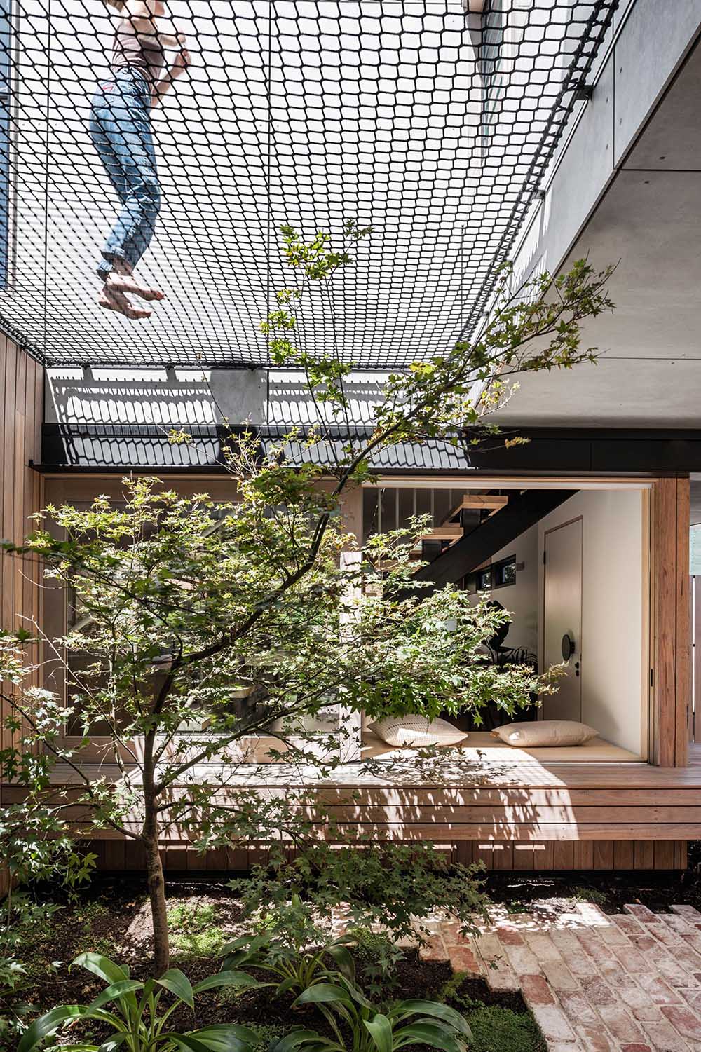 A compact courtyard with brick and greenery connects to a playful netted space above, turning unused areas into functional zones.