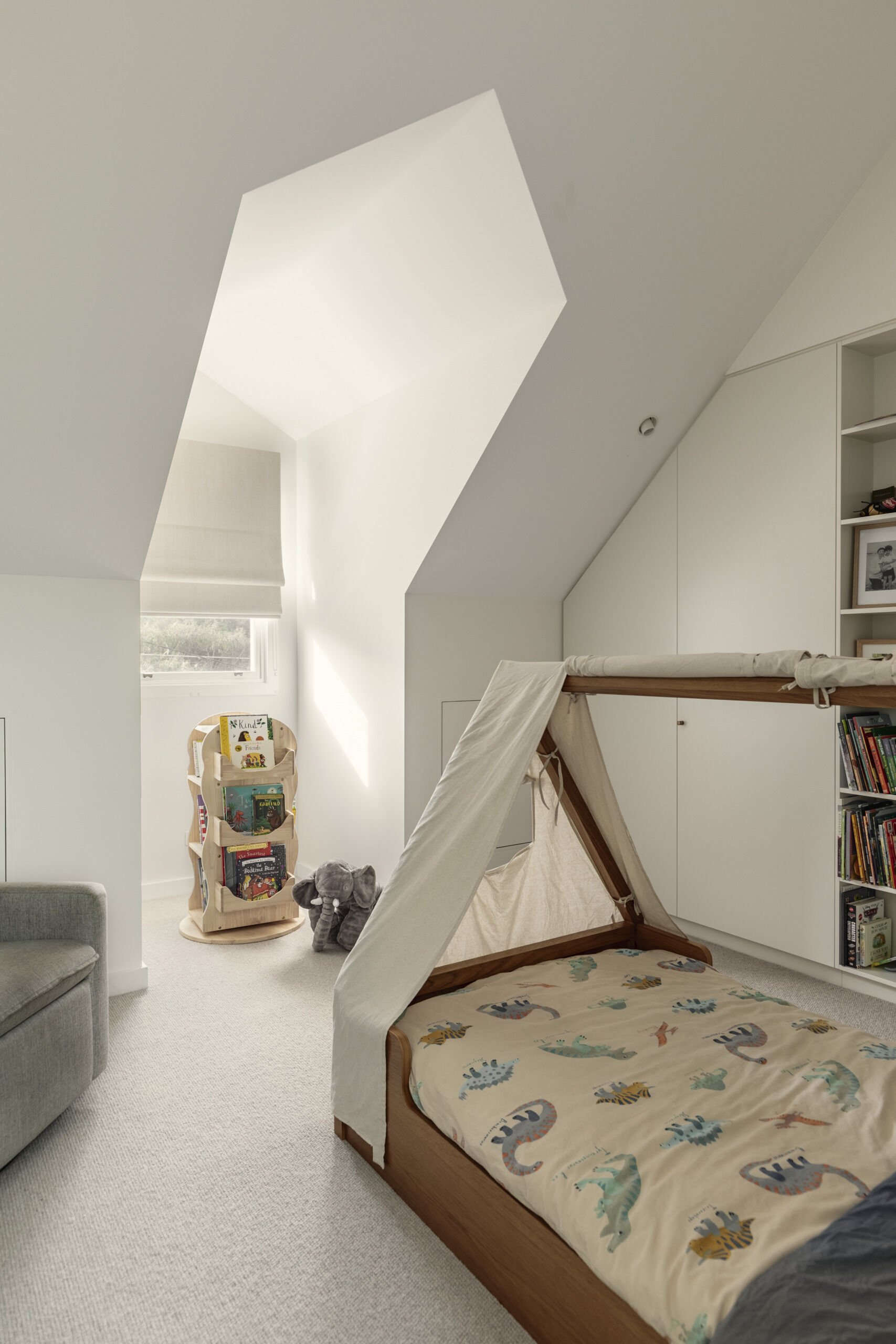 This child's bedroom feels bright, calm, and full of quiet imagination, with its sculptural sloped ceiling, soft white walls, and pale carpet keeping everything light and airy.