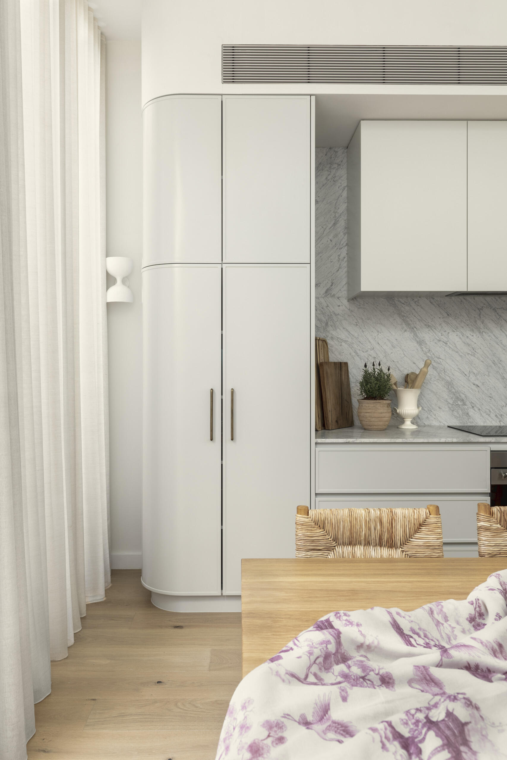 The kitchen follows a minimalist approach, with clean lines and a restrained palette. Natural stone countertops and backsplash, cabinets with curved designs, and timber from the island introduce texture and depth without relying on bold color.