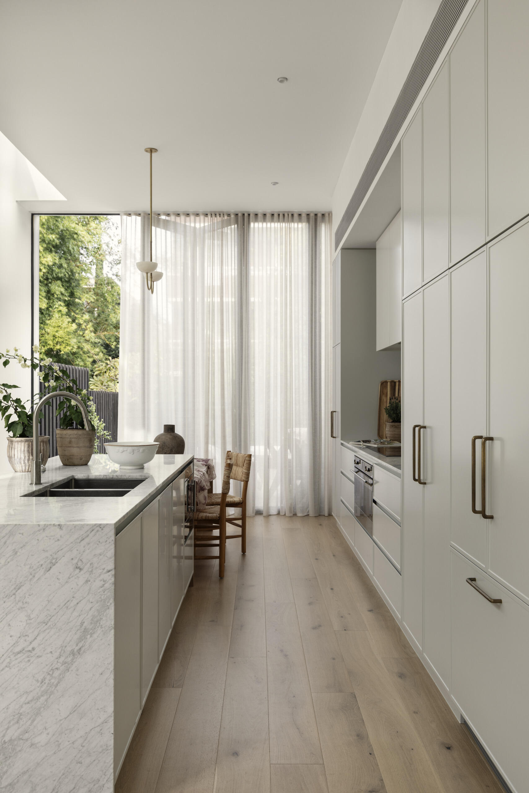 The kitchen follows a minimalist approach, with clean lines and a restrained palette. Natural stone countertops and backsplash, cabinets with curved designs, and timber from the island introduce texture and depth without relying on bold color.