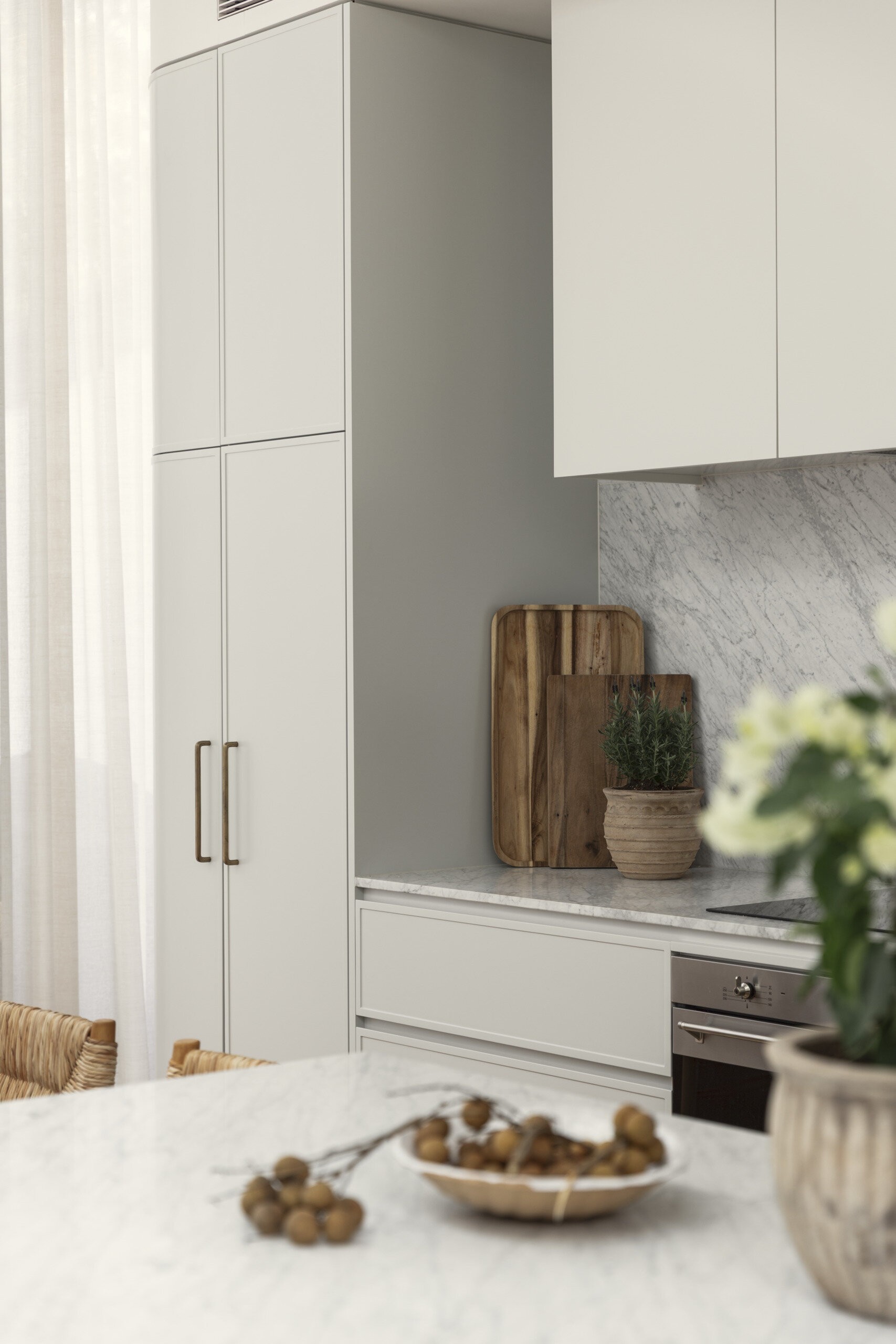 The kitchen follows a minimalist approach, with clean lines and a restrained palette. Natural stone countertops and backsplash, cabinets with curved designs, and timber from the island introduce texture and depth without relying on bold color.