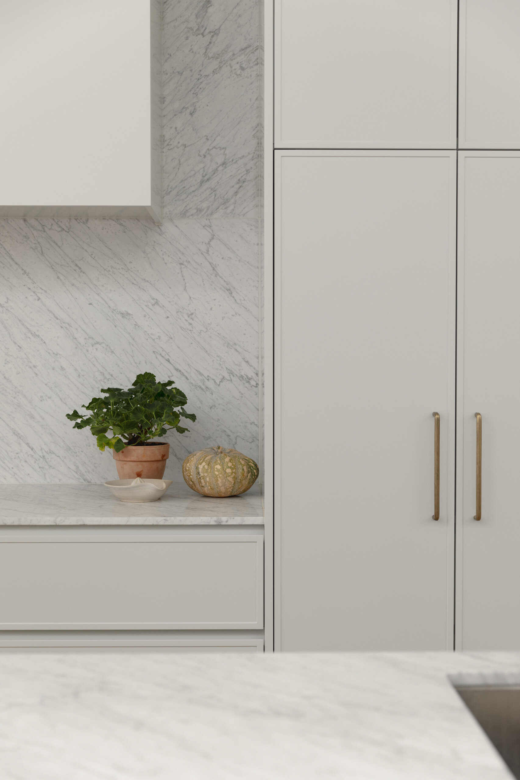 The kitchen follows a minimalist approach, with clean lines and a restrained palette. Natural stone countertops and backsplash, cabinets with curved designs, and timber from the island introduce texture and depth without relying on bold color.