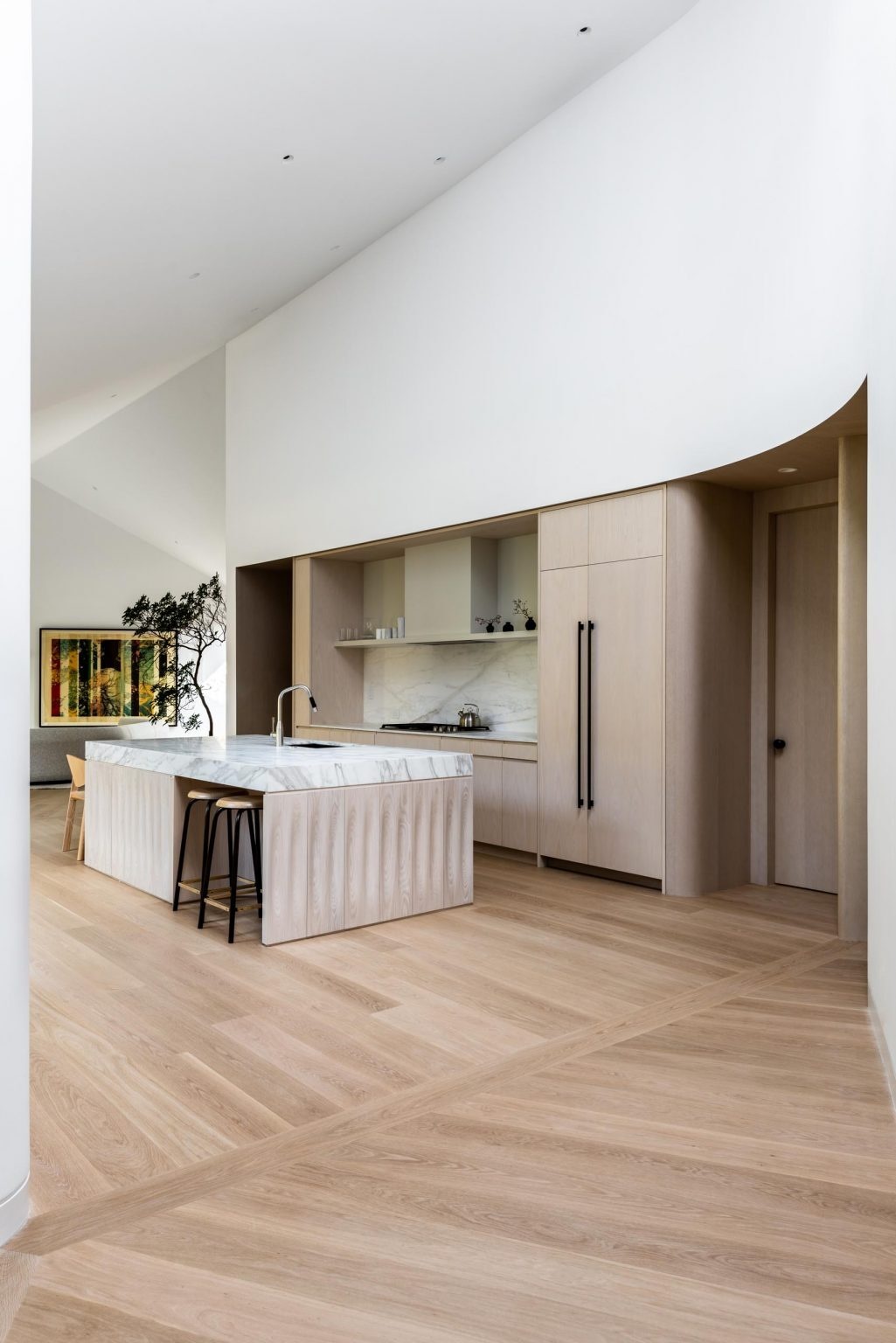 A minimalist kitchen combines white oak floors, wood cabinetry, black hardware, and a statement marble island.