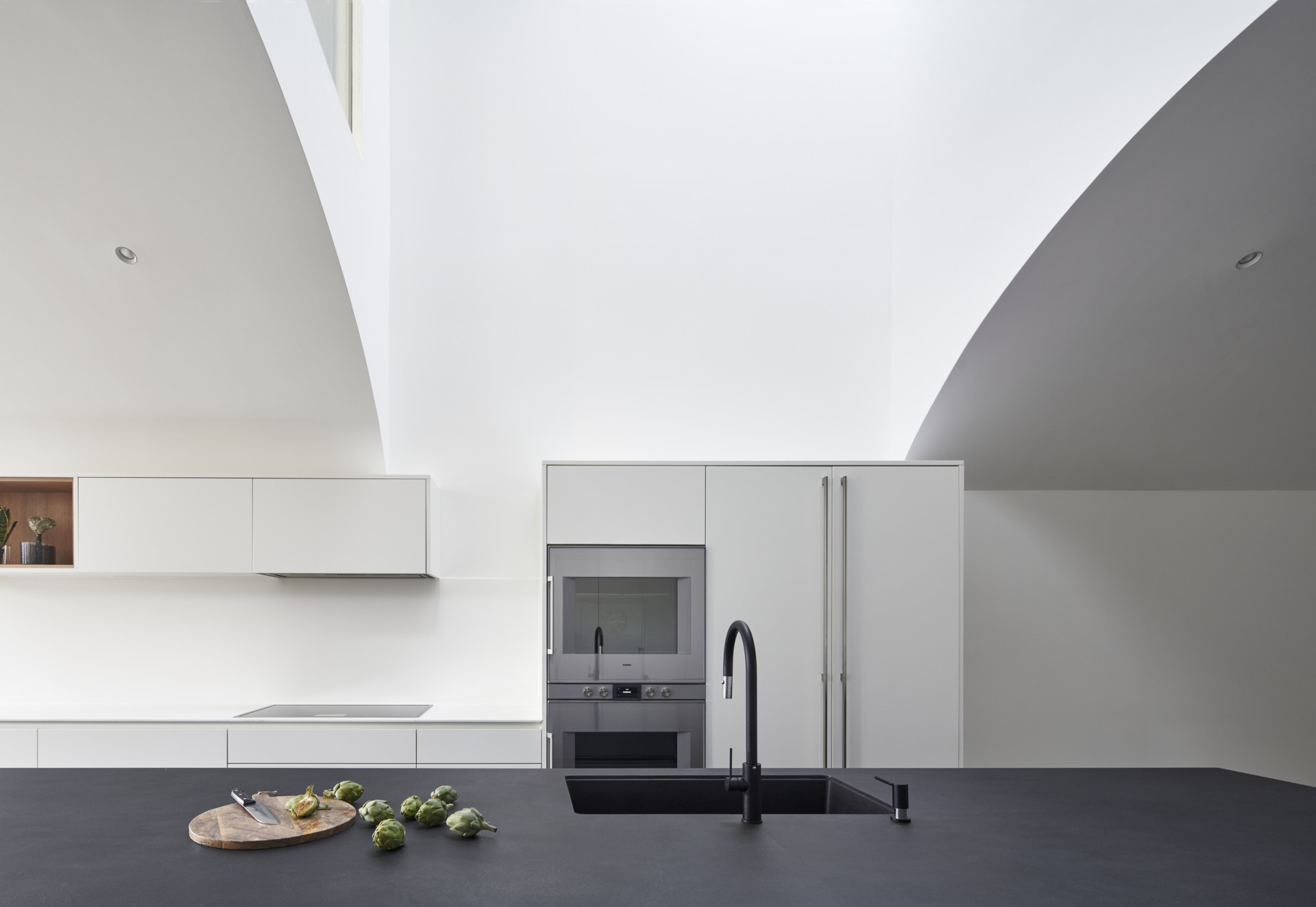 A minimalist white kitchen paired with a matte blue island creates a clean yet striking focal point under a curved ceiling.