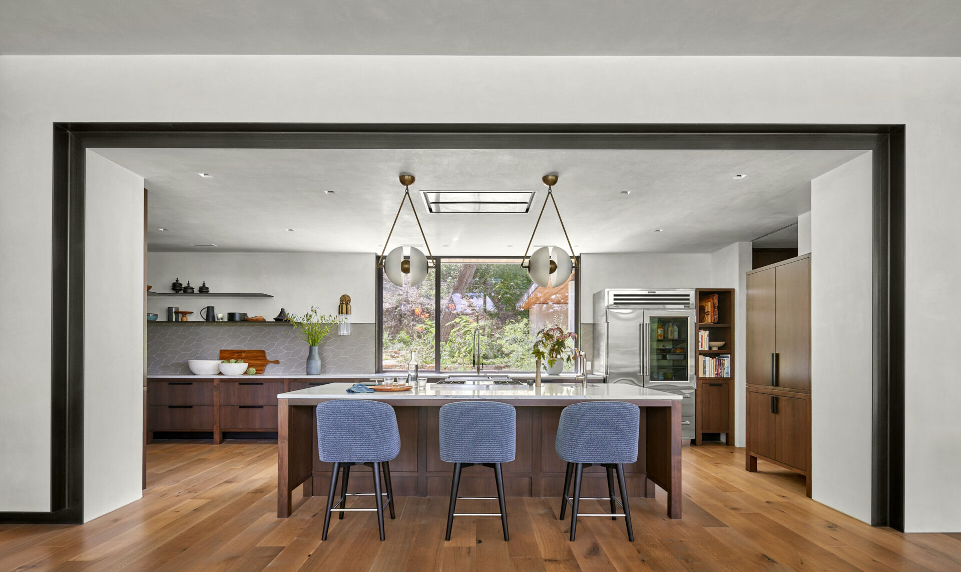 A modern kitchen features cabinetry on wooden legs, a glass-front refrigerator, and a custom armoire for coffee equipment.