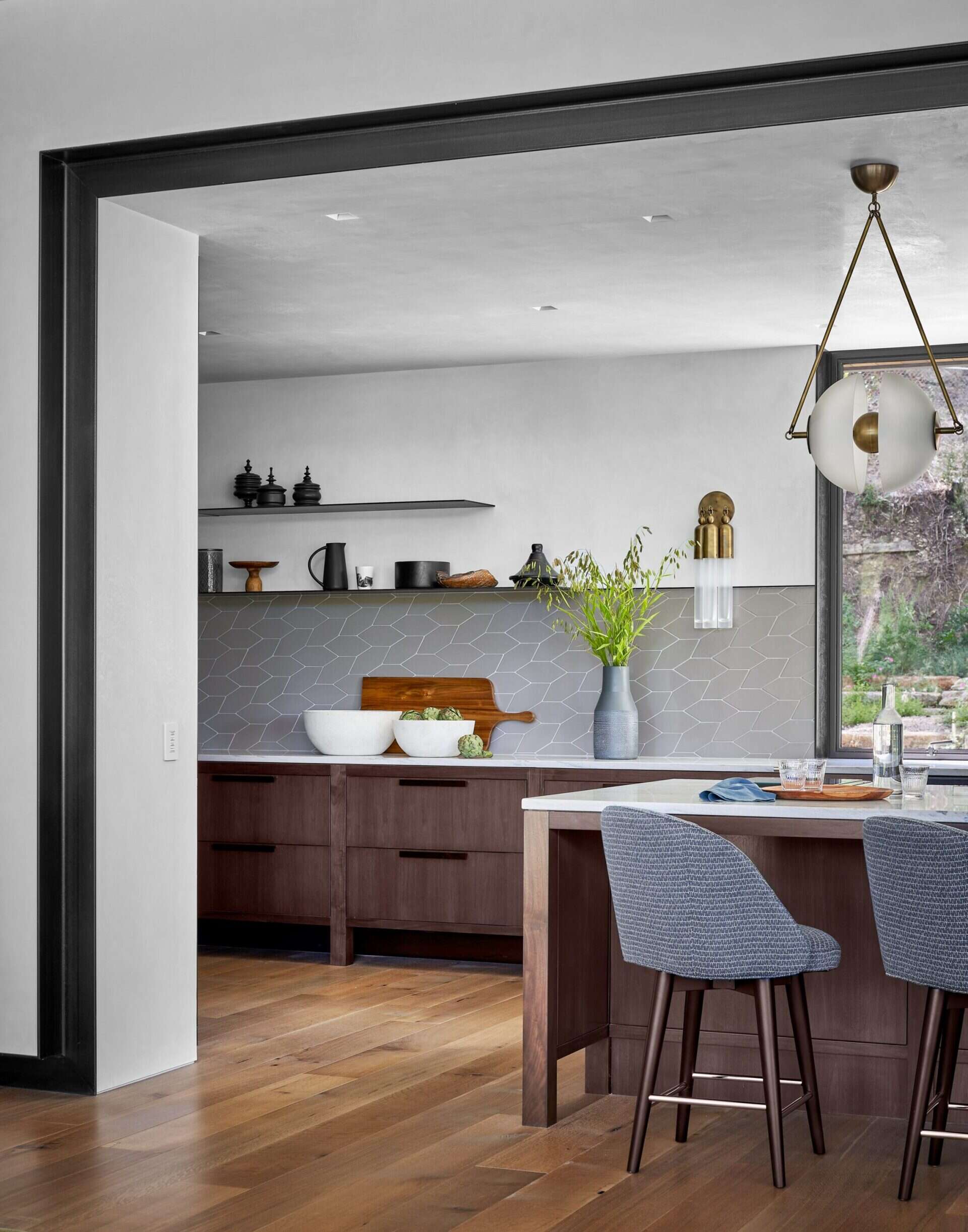 A modern kitchen features cabinetry on wooden legs, a glass-front refrigerator, and a custom armoire for coffee equipment.