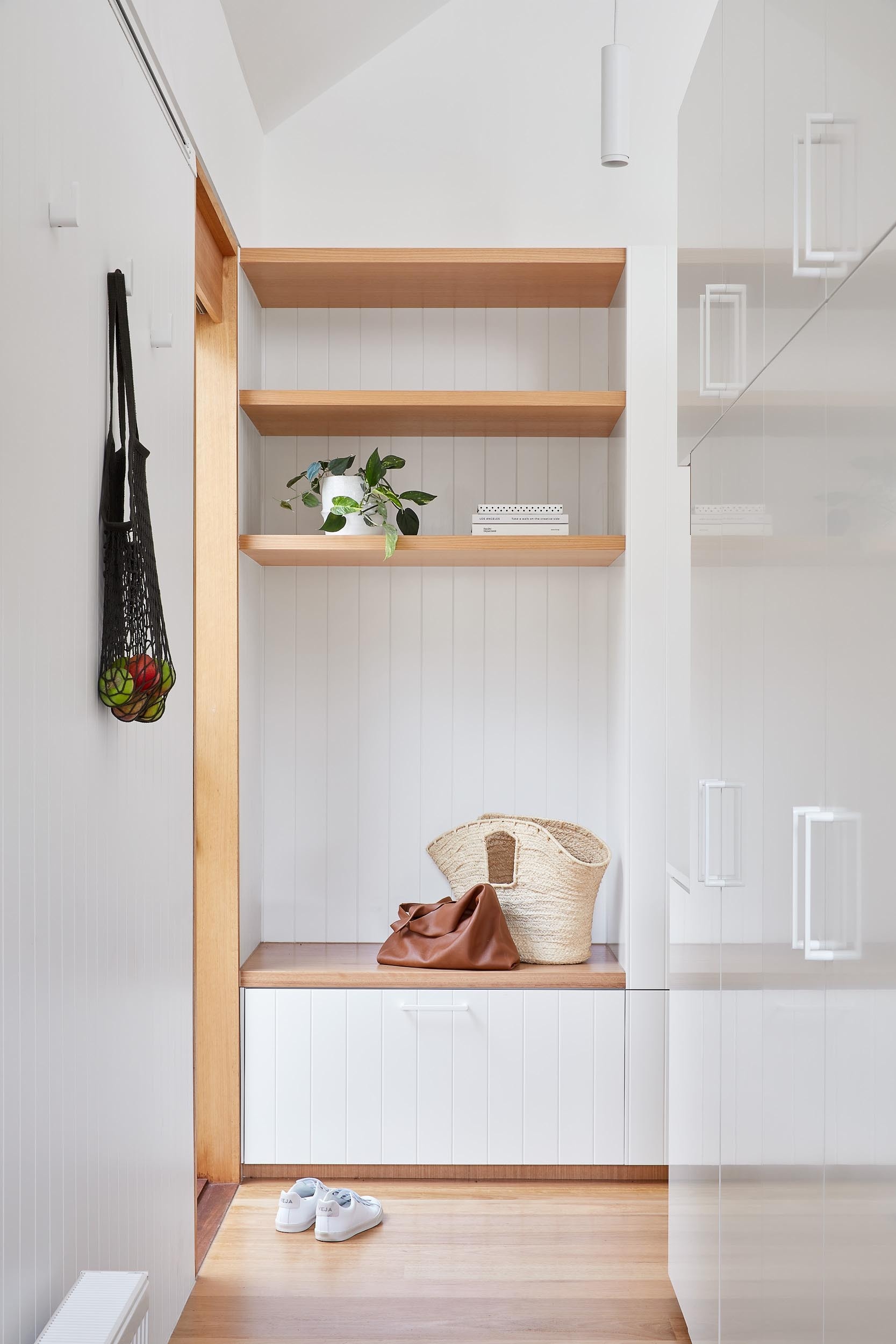 Hidden behind the main wall of cabinetry, a laundry room continues the material palette with a timber bench and open shelving, keeping utility spaces consistent with the rest of the home.