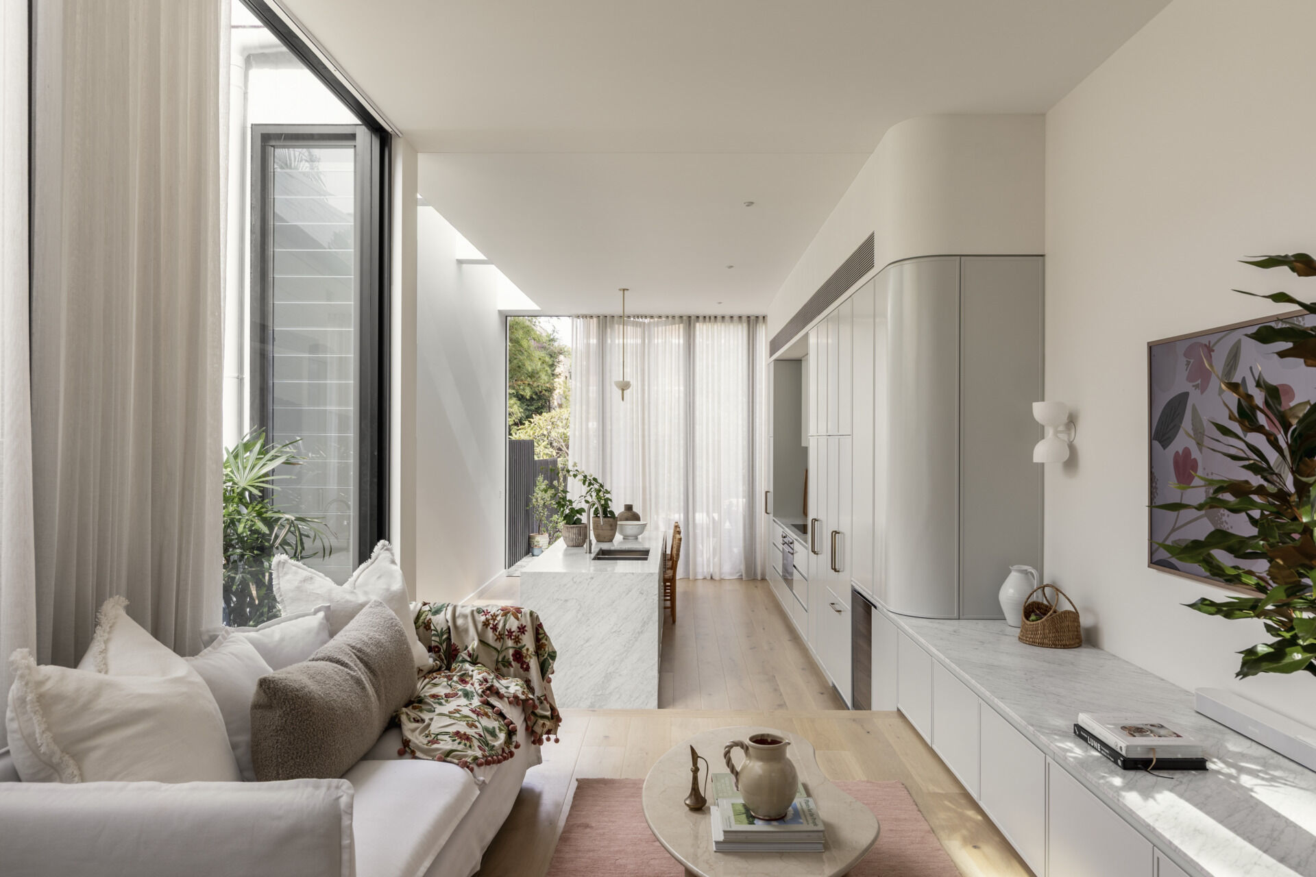 The living room sits slightly above the kitchen, offering a more relaxed setting within the open-plan layout. Natural light filters in from multiple directions, softening the space and highlighting the material palette. It feels connected to everything around it while still having its own identity.
