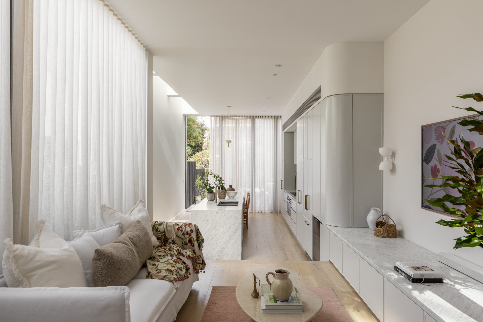 The living room sits slightly above the kitchen, offering a more relaxed setting within the open-plan layout. Natural light filters in from multiple directions, softening the space and highlighting the material palette. It feels connected to everything around it while still having its own identity.