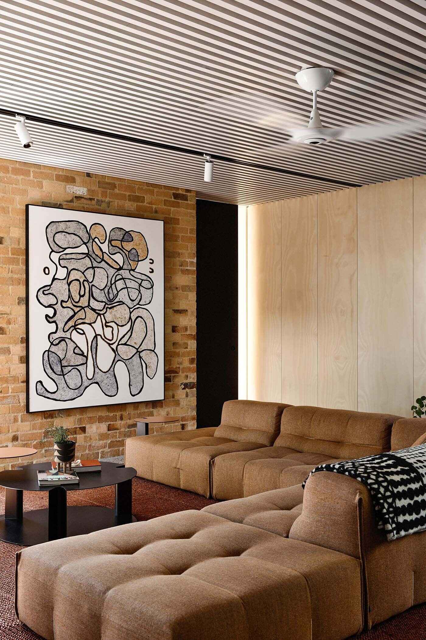 A white slatted ceiling, large sofa, and hidden workspace define a living area that balances openness and function.