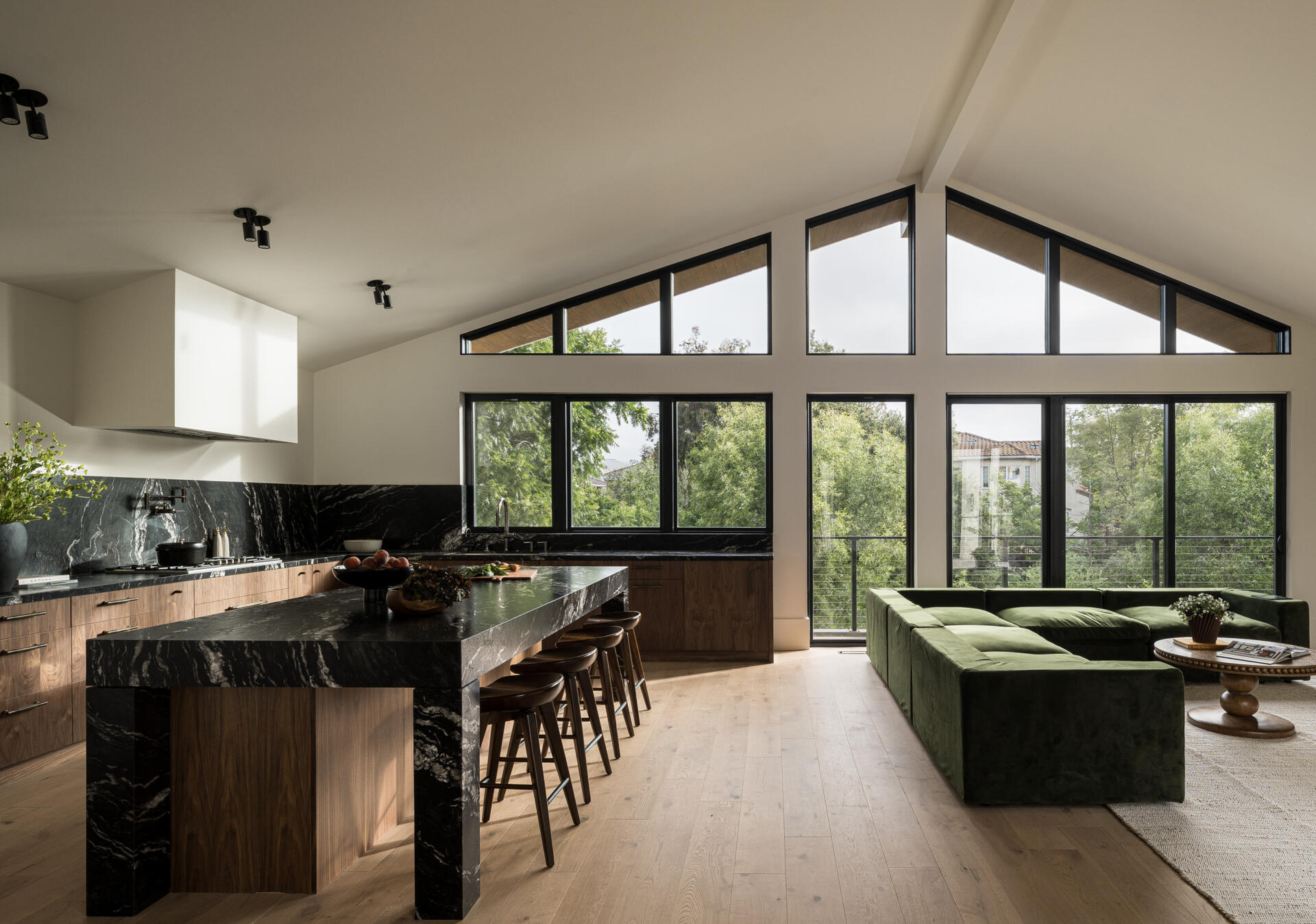 At the rear, the living room opens toward dense greenery along the edge of the lot. A large window wall frames these views, giving the space a calm outlook while maintaining privacy from nearby homes.
