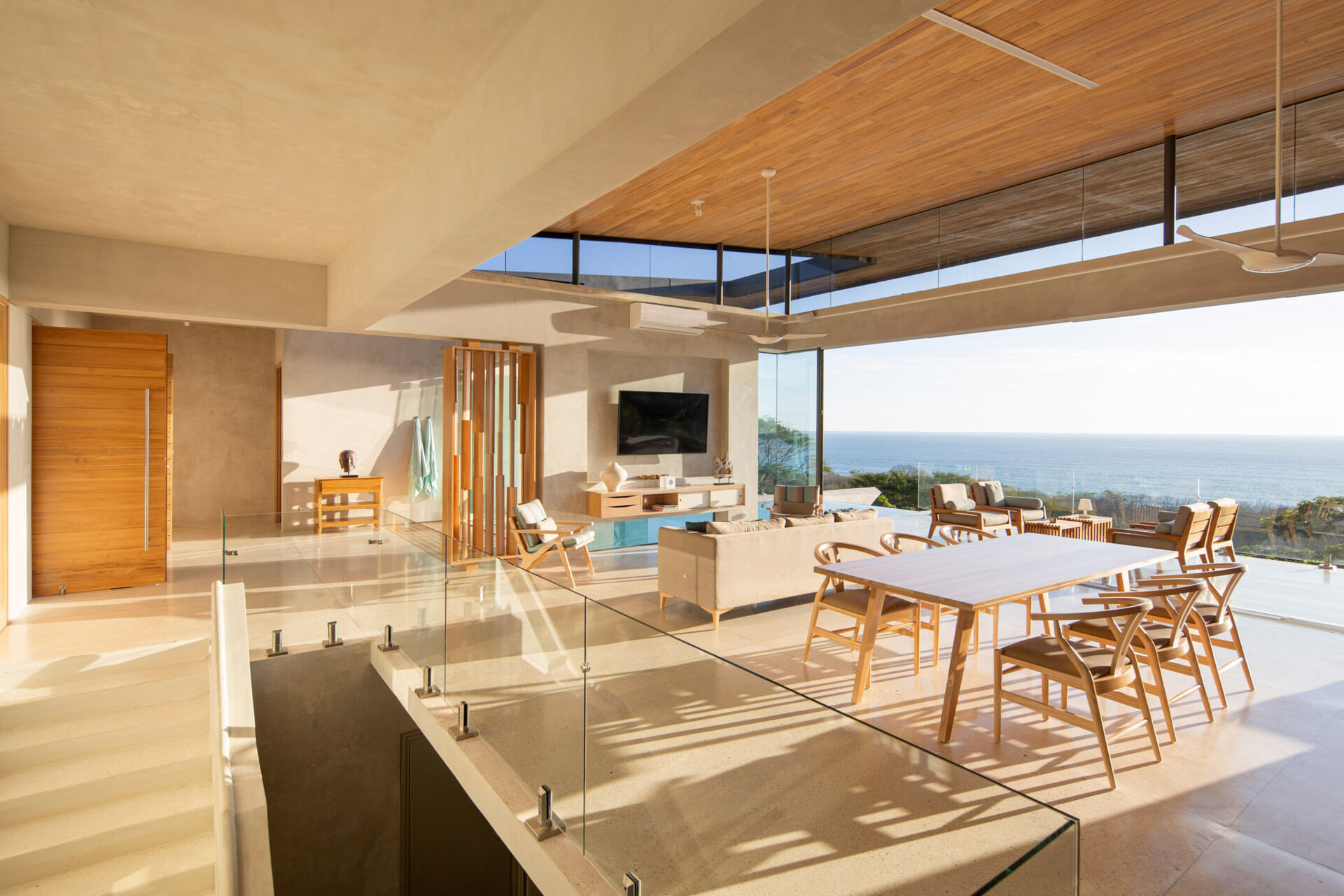An open plan living space with a floating wood ceiling and sliding glass walls that open fully to a shaded balcony.