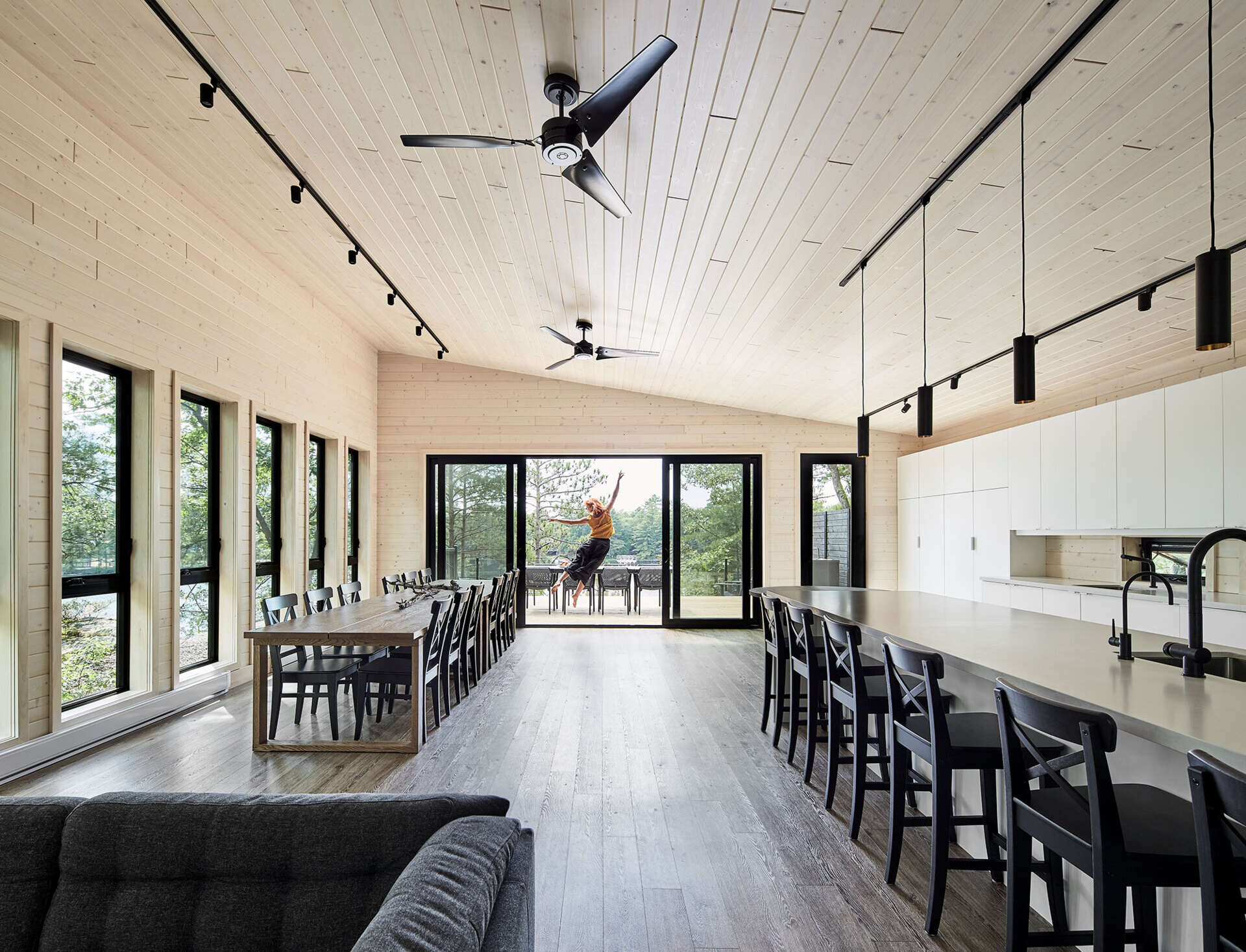 An open-plan upper level with a fireplace lounge, multiple dining tables, and a bold black-and-white kitchen designed for large family gatherings.