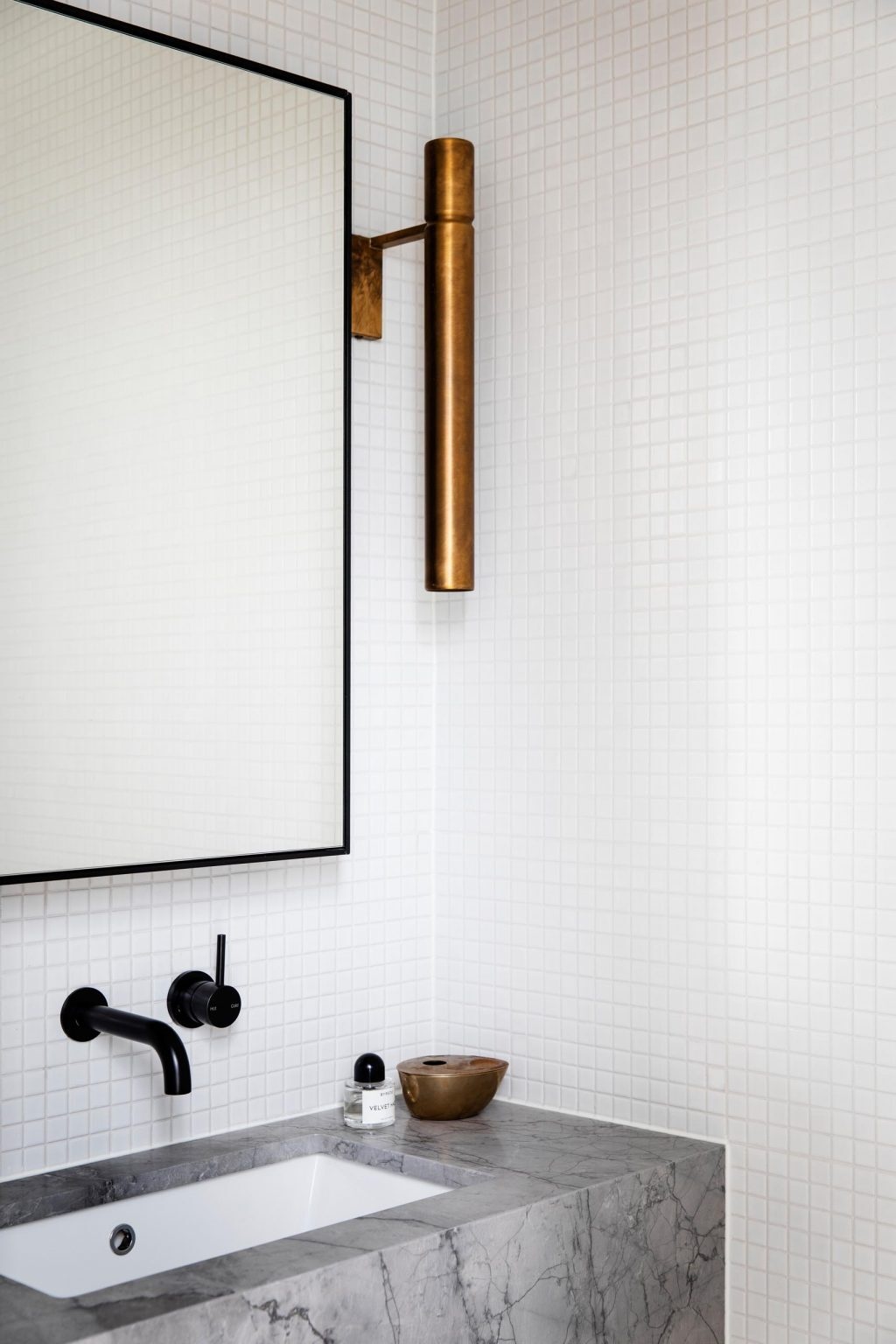 A powder room mixes white tiles with a stone vanity, black mirror frame, and brass lighting for a subtle contrast.