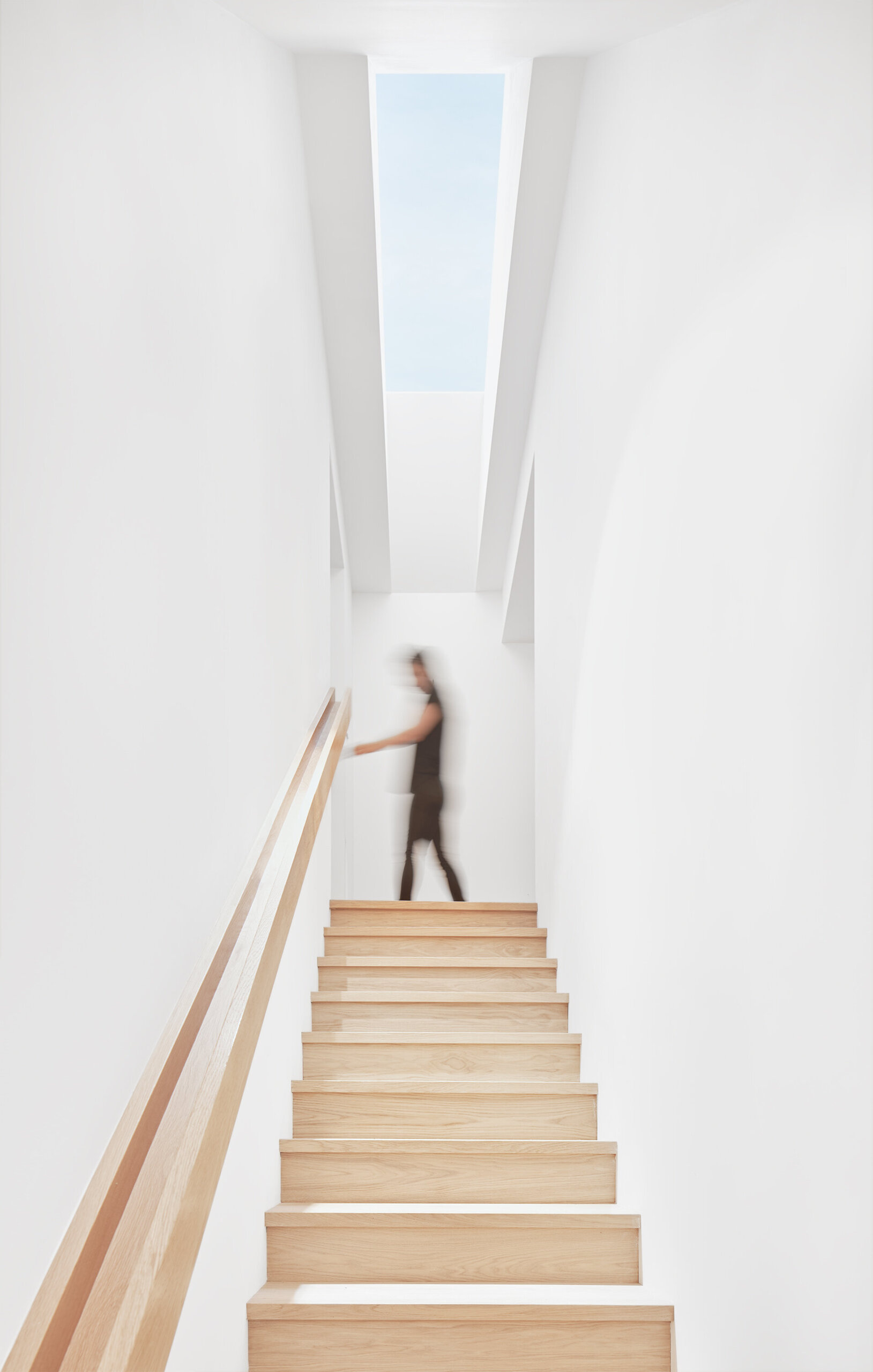 Una escalera de paredes blancas proporciona una transición limpia entre niveles, conectando los espacios sociales con las habitaciones privadas de arriba.