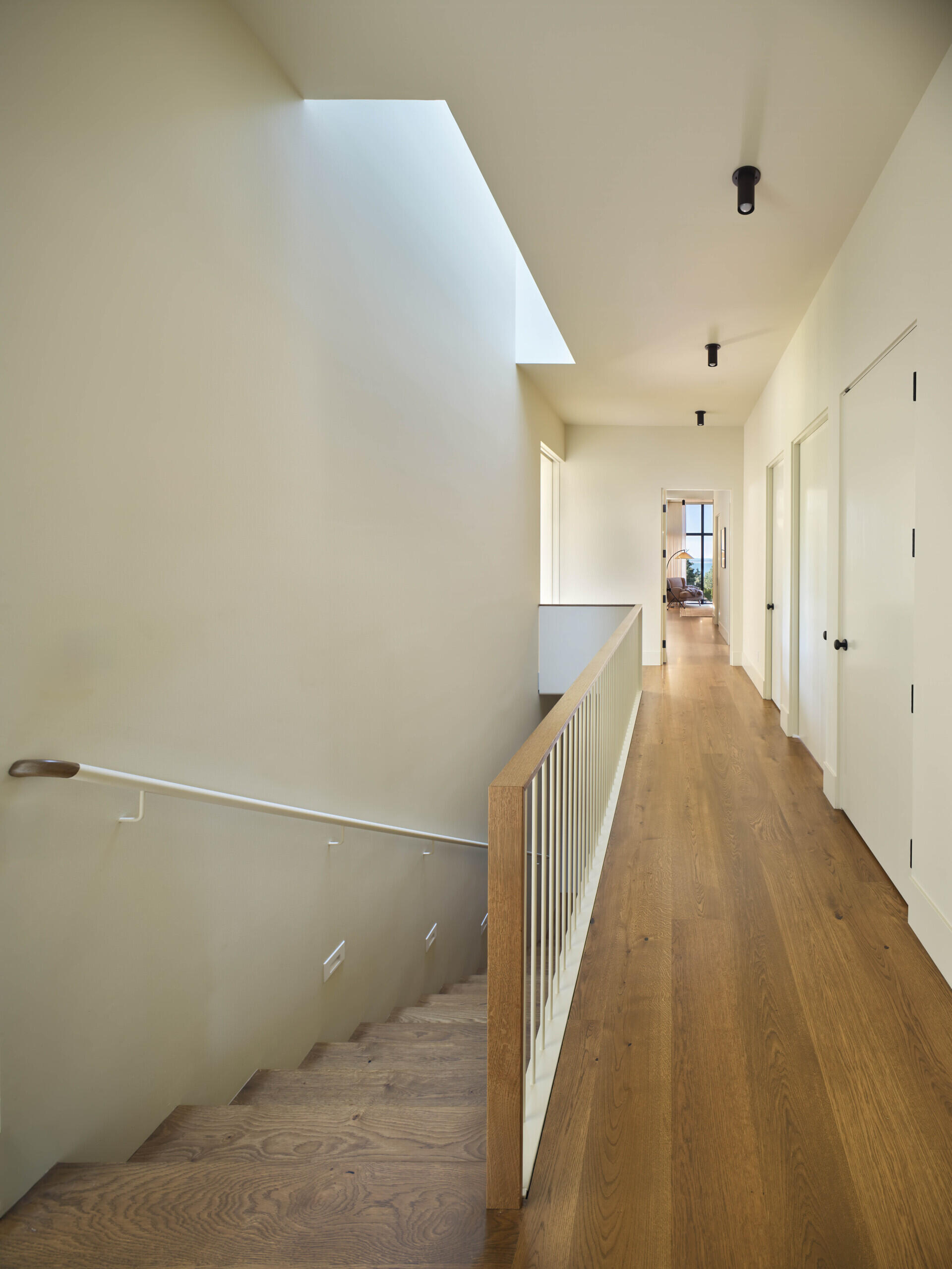 A wood staircase connects the social areas of the home to the more private spaces. Above, a skylight brings daylight down through the stair, brightening the lower level.