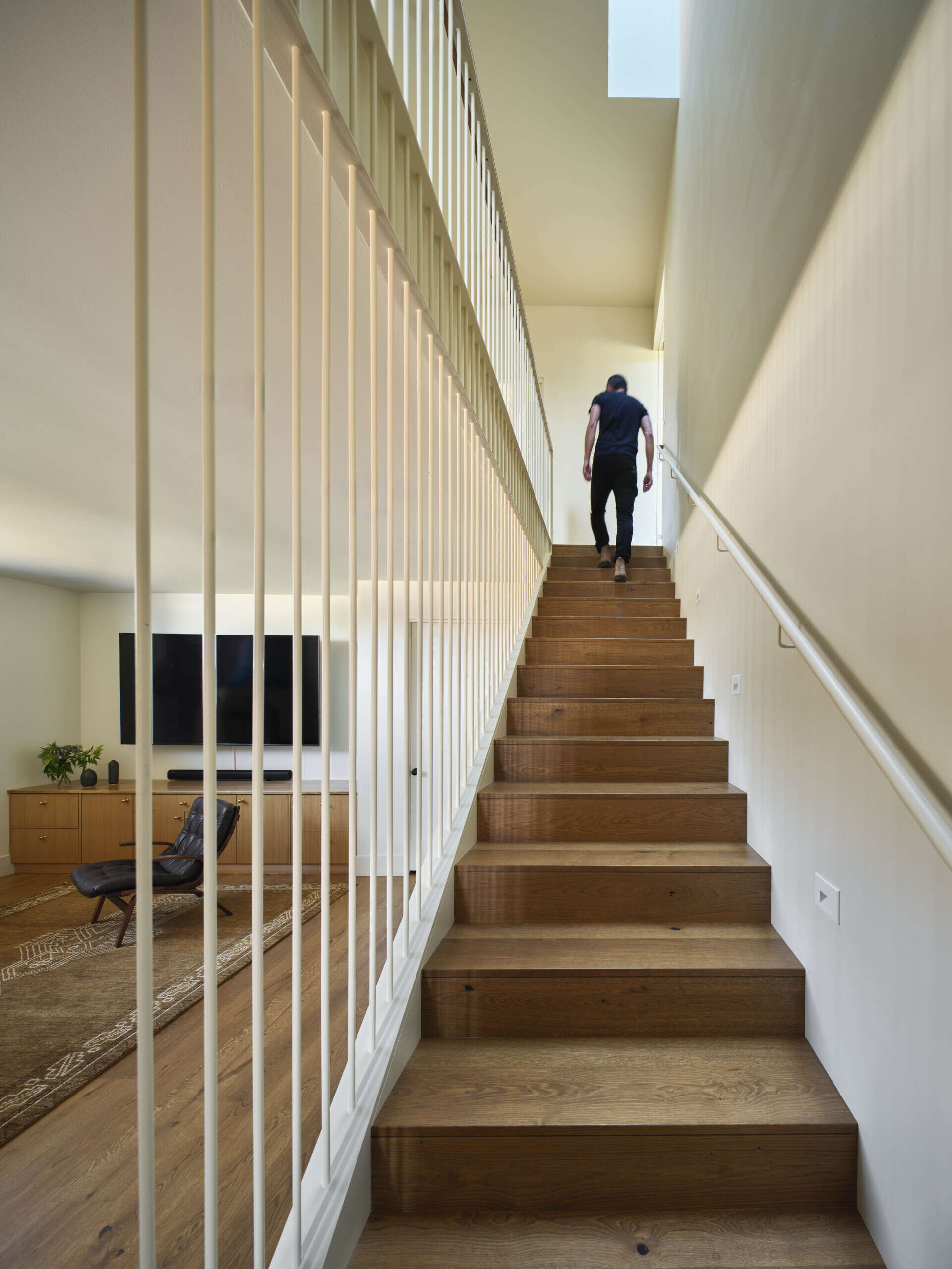A wood staircase connects the social areas of the home to the more private spaces. Above, a skylight brings daylight down through the stair, brightening the lower level.