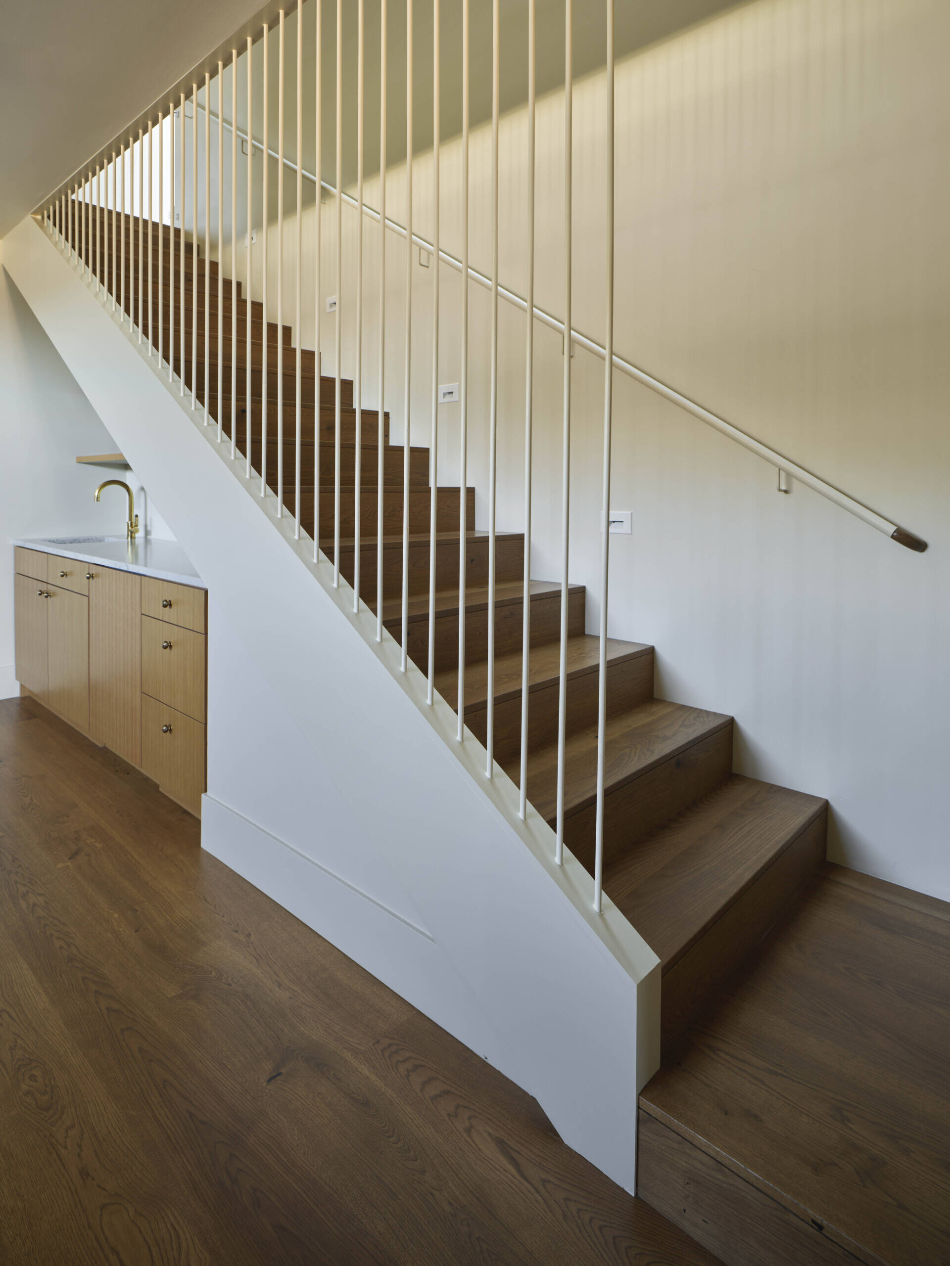 A wood staircase connects the social areas of the home to the more private spaces. Above, a skylight brings daylight down through the stair, brightening the lower level.