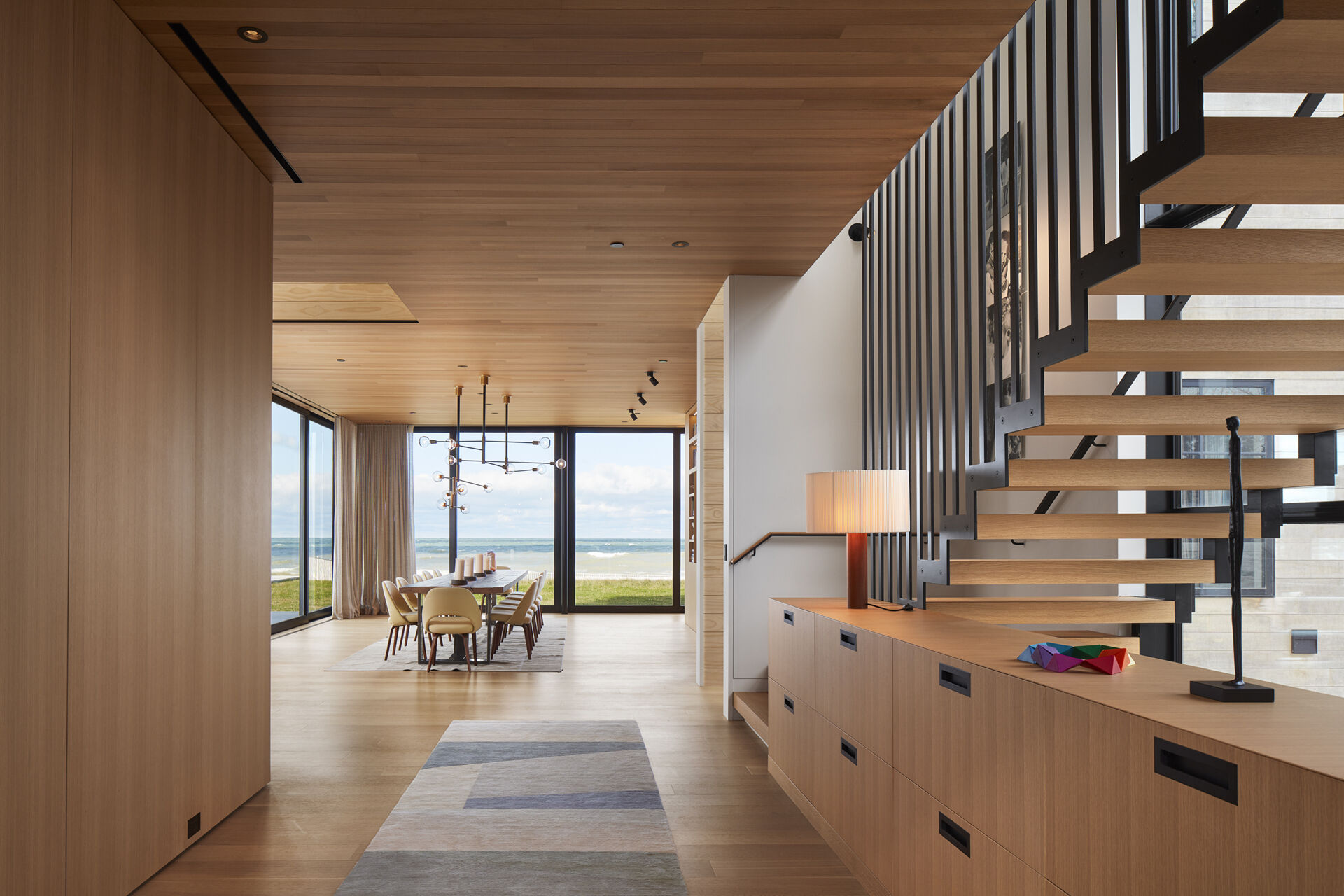 A floating steel staircase with oak treads adds a bold architectural feature to the home. Built-in cabinetry nearby provides practical storage, keeping the overall look clean and uncluttered.