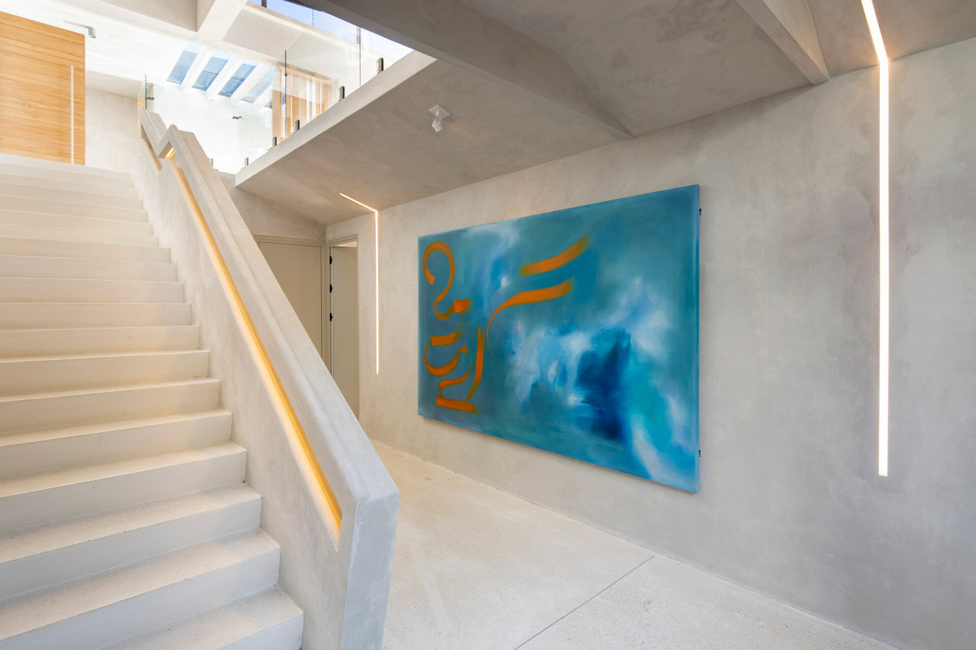 A concrete staircase with integrated lighting leads to lower-level bedrooms, contrasting solid spaces below with open living areas above.