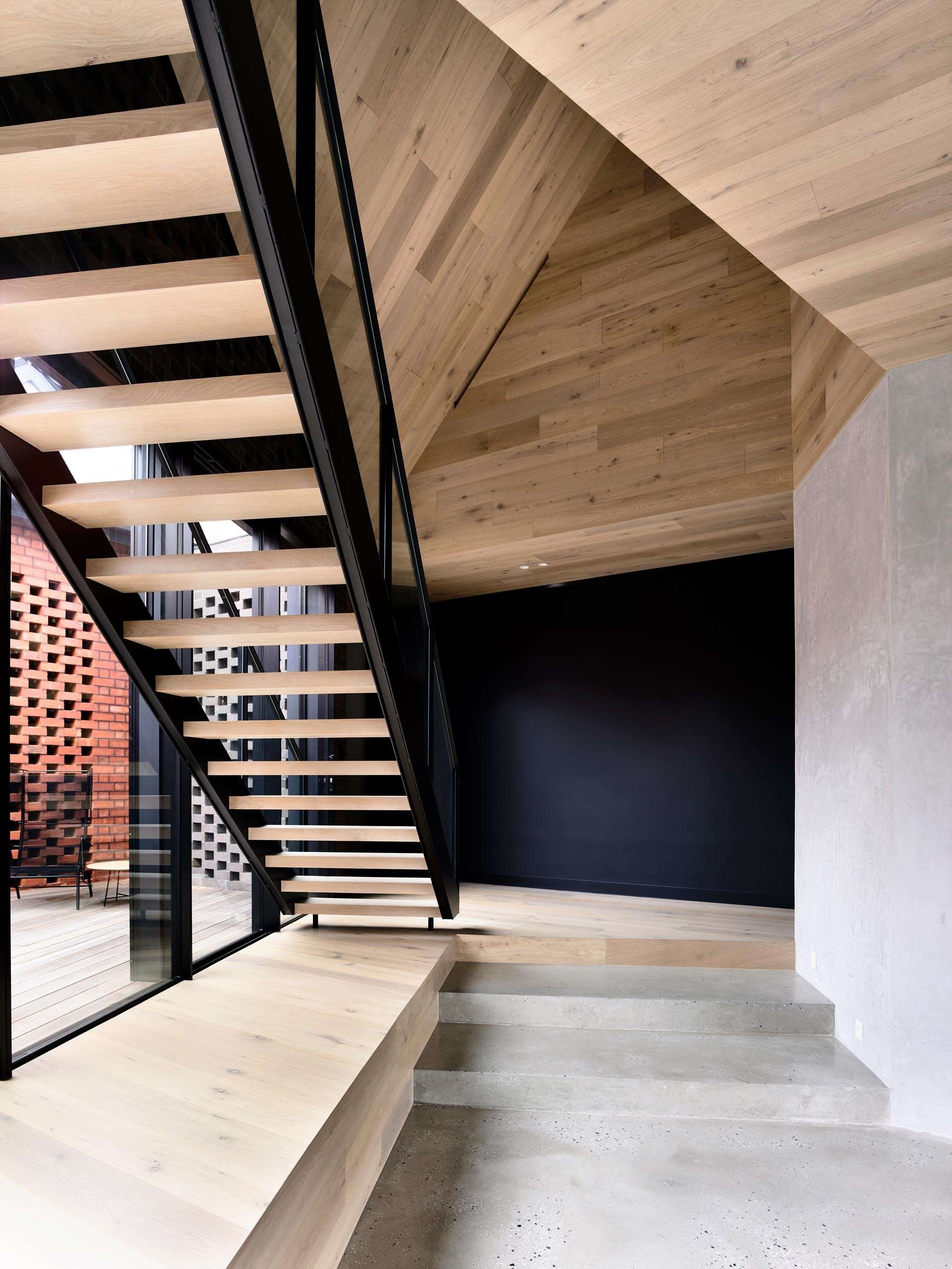 A staircase sits beneath an origami-style timber ceiling, turning a functional element into a striking architectural feature.