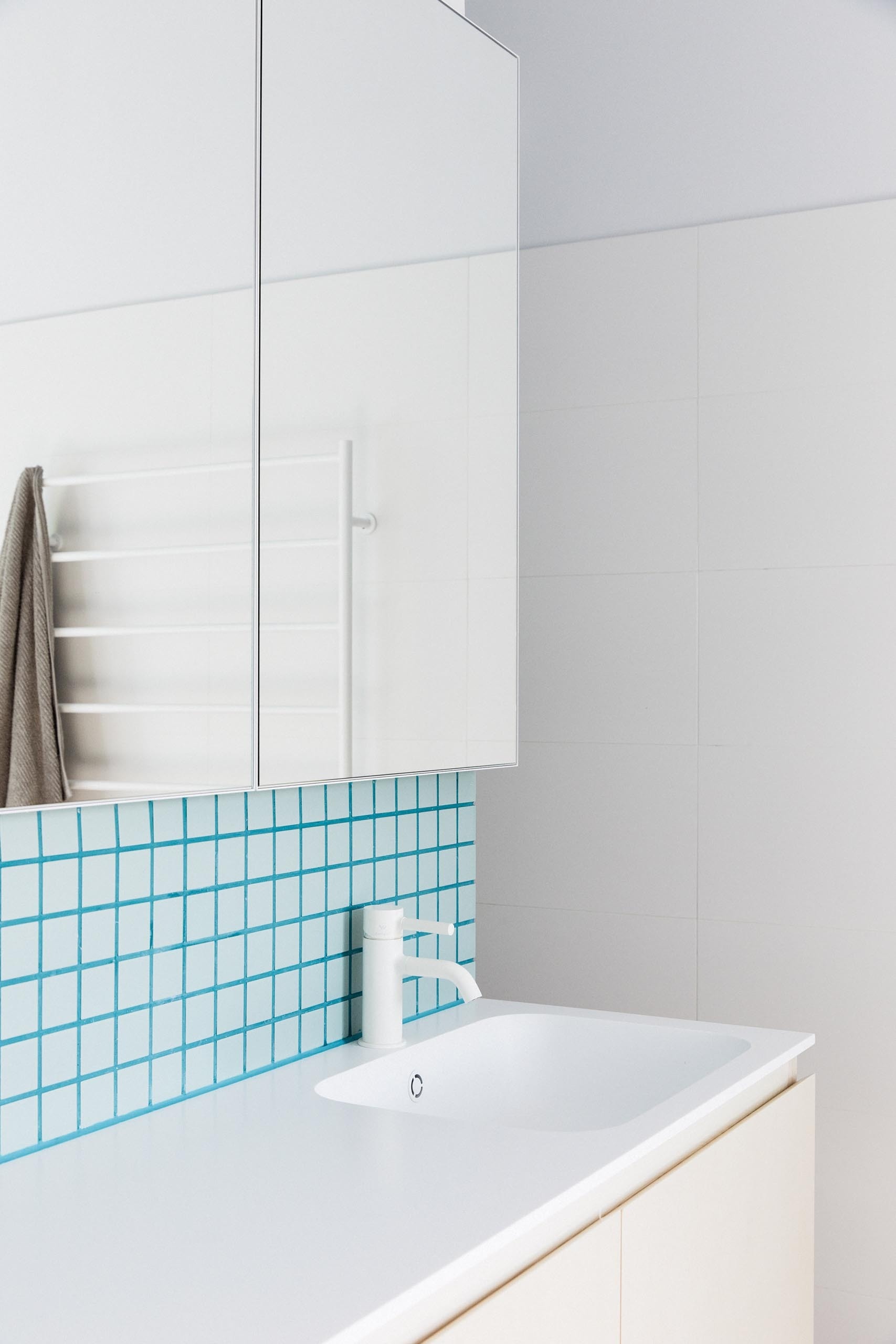 This modern bathroom pairs white walls with soft blue-green tiles and matching grout, creating a clean, contemporary feel.