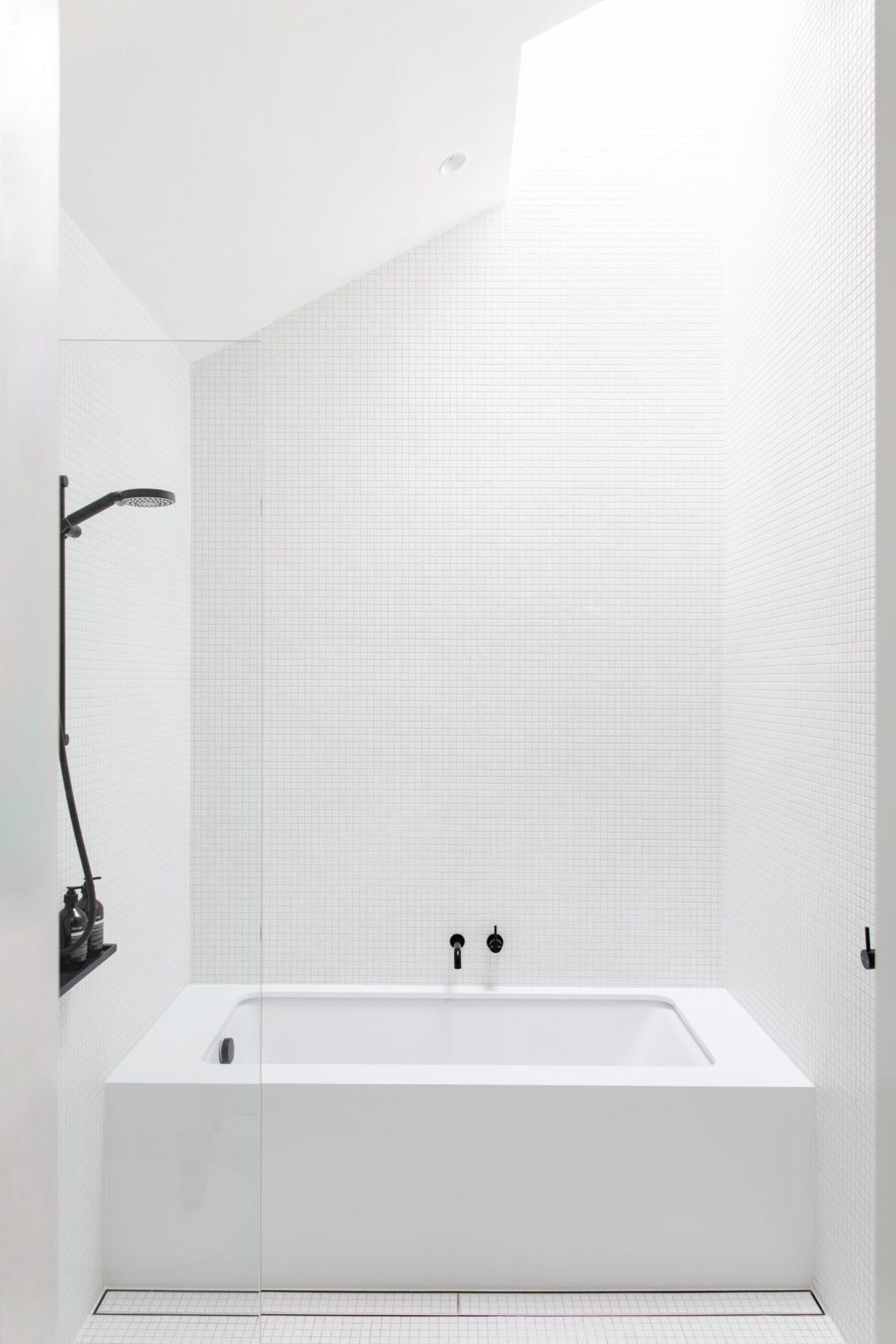 White square tiles, black accents, and a skylight create a bright, minimalist bathroom design.