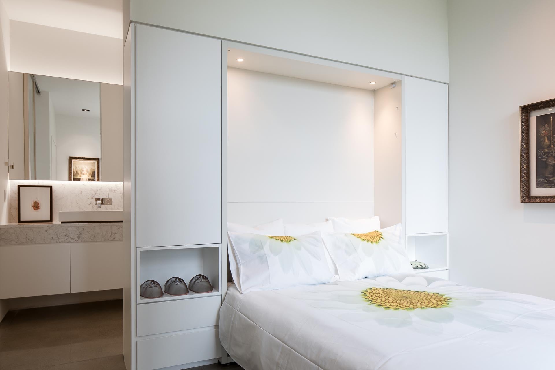In this bedroom, custom cabinetry wraps around the headboard, creating separation between the sleeping area and the en-suite bathroom while maintaining a clean, integrated look.