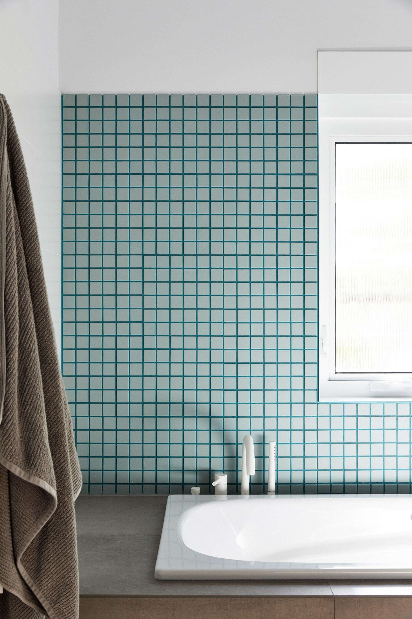 This modern bathroom pairs white walls with soft blue-green tiles and matching grout, creating a clean, contemporary feel.