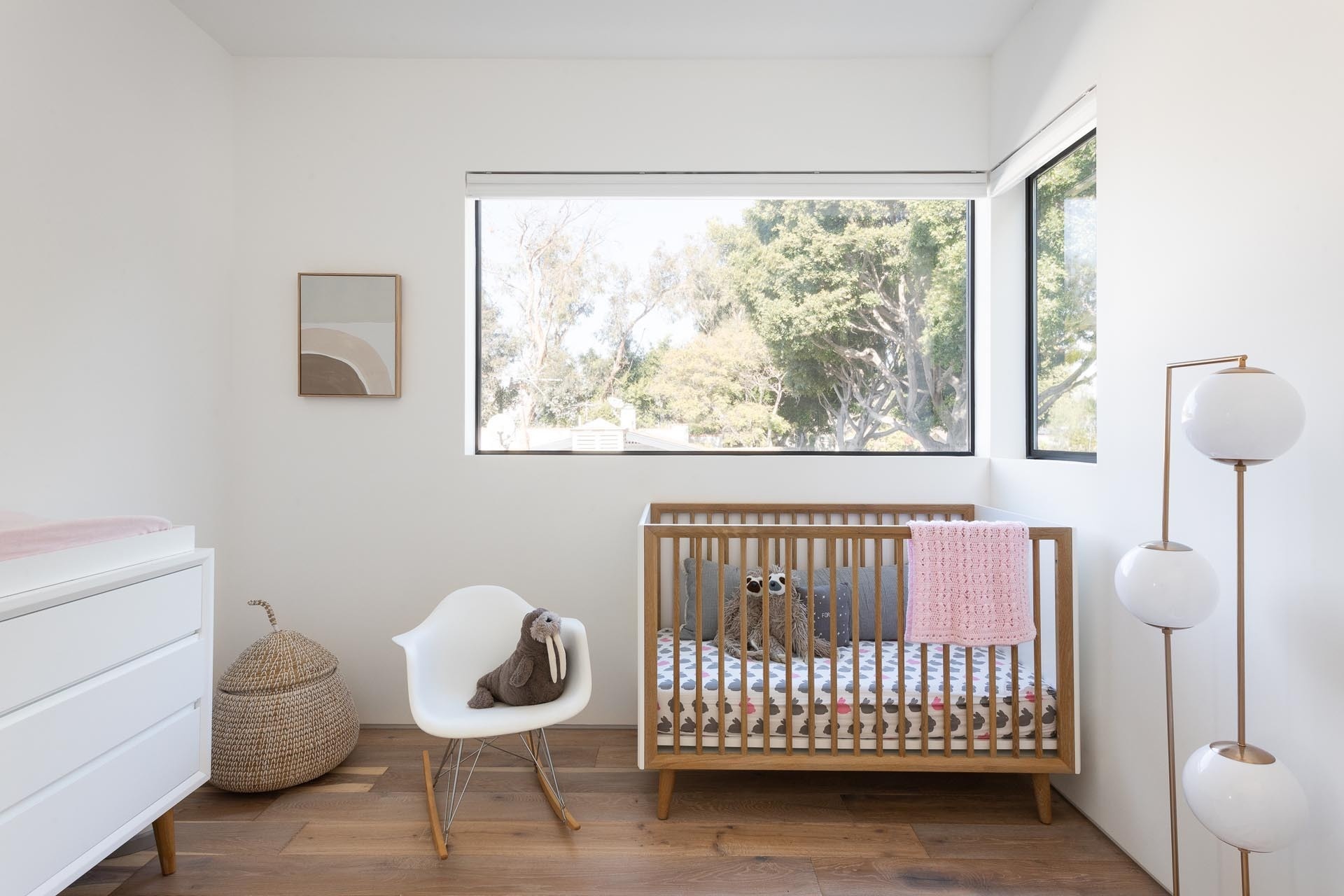 A bright nursery with large windows and simple furnishings creates a calm and modern space for growing families.