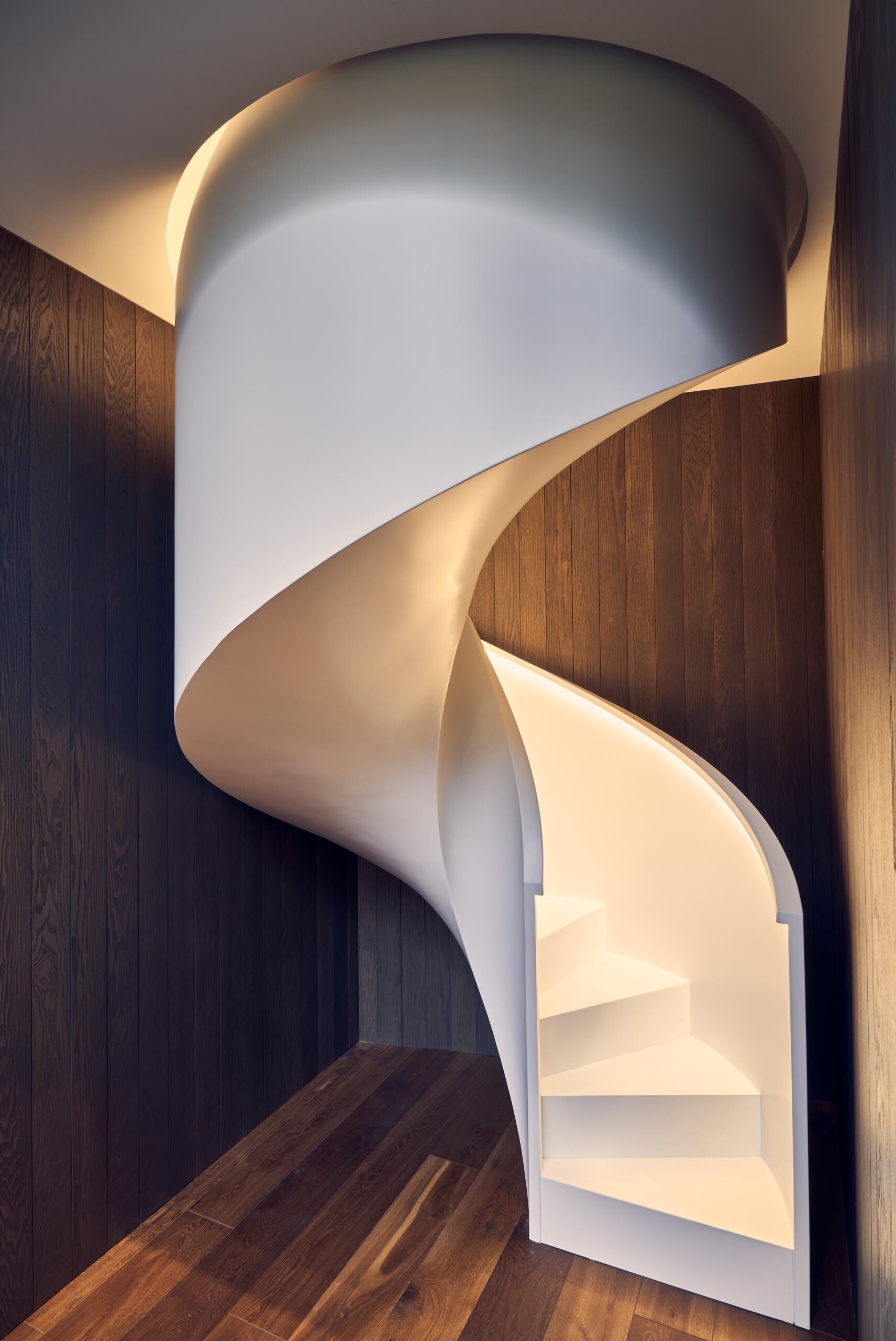 A white spiral staircase with hidden lighting becomes a sculptural centerpiece that ties both levels together.