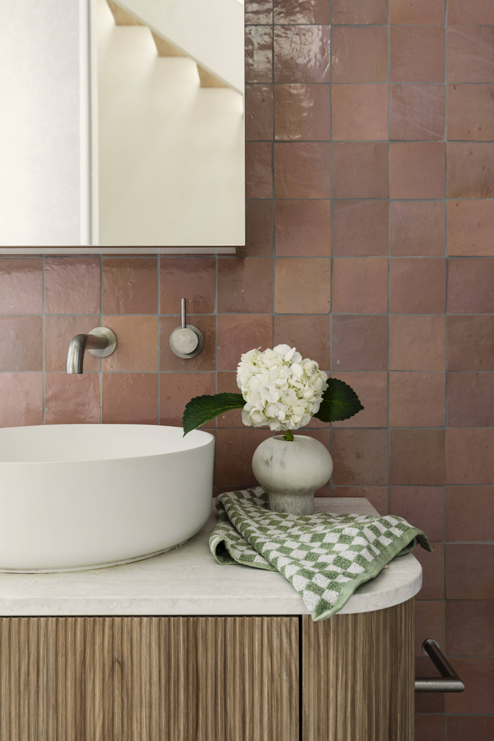 This guest bathroom sits nearby and pairs earthy terracotta-colored tile with soft gray surfaces for a look that feels warm and grounded. The ribbed wood vanity adds texture, while the round vessel sink keeps the lines clean and sculptural.