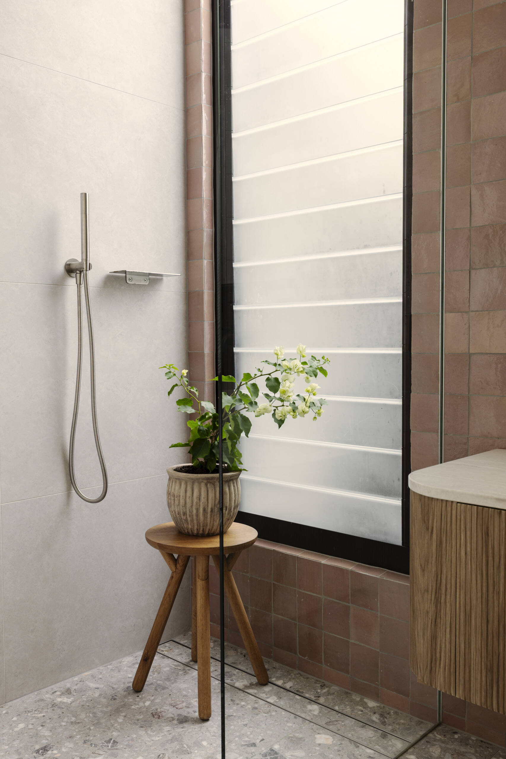 This guest bathroom sits nearby and pairs earthy terracotta-colored tile with soft gray surfaces for a look that feels warm and grounded. The ribbed wood vanity adds texture, while the round vessel sink keeps the lines clean and sculptural.
