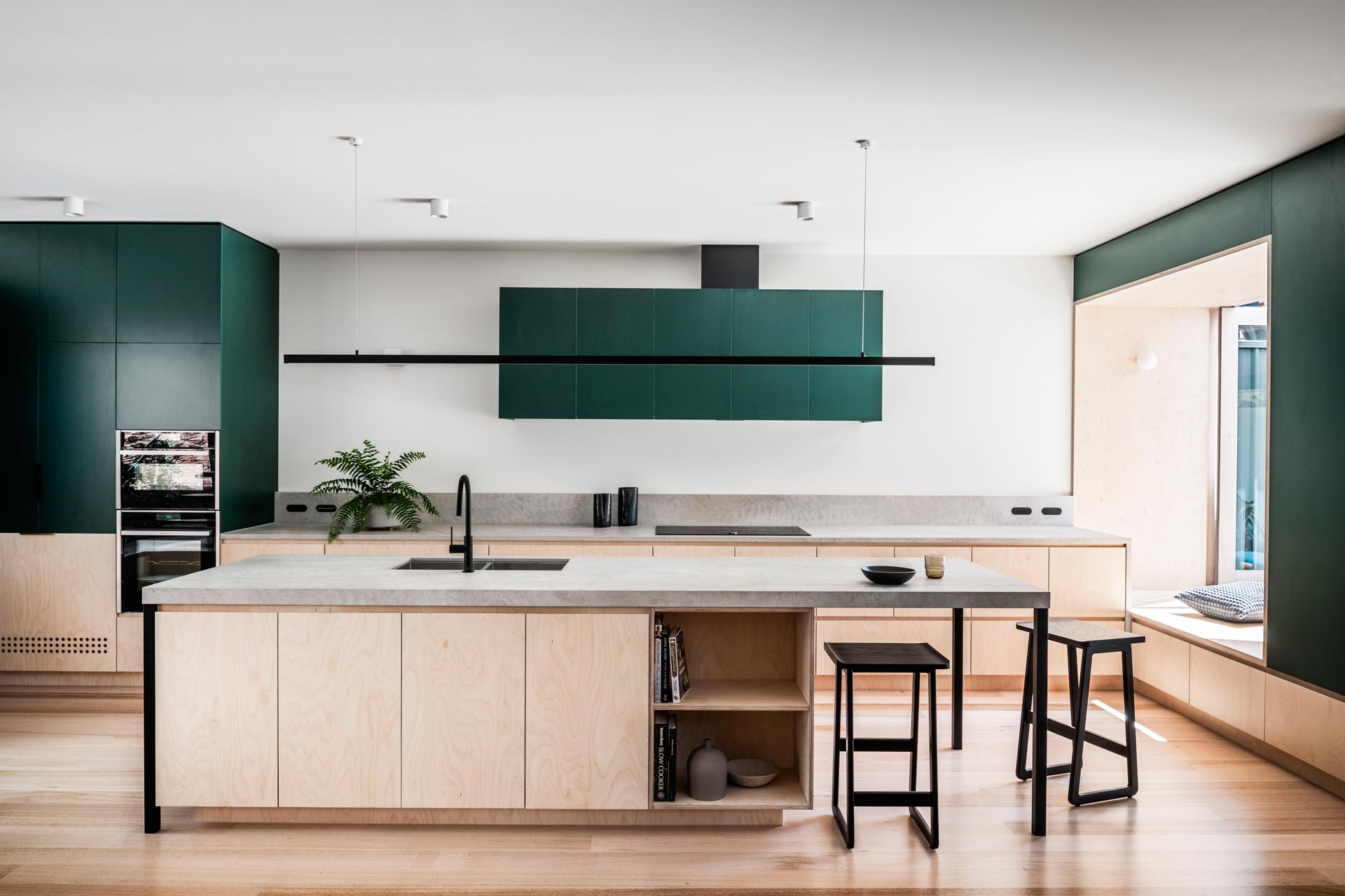 Deep green kitchen cabinets paired with wood and stone textures create a warm, modern space centered around a functional island.